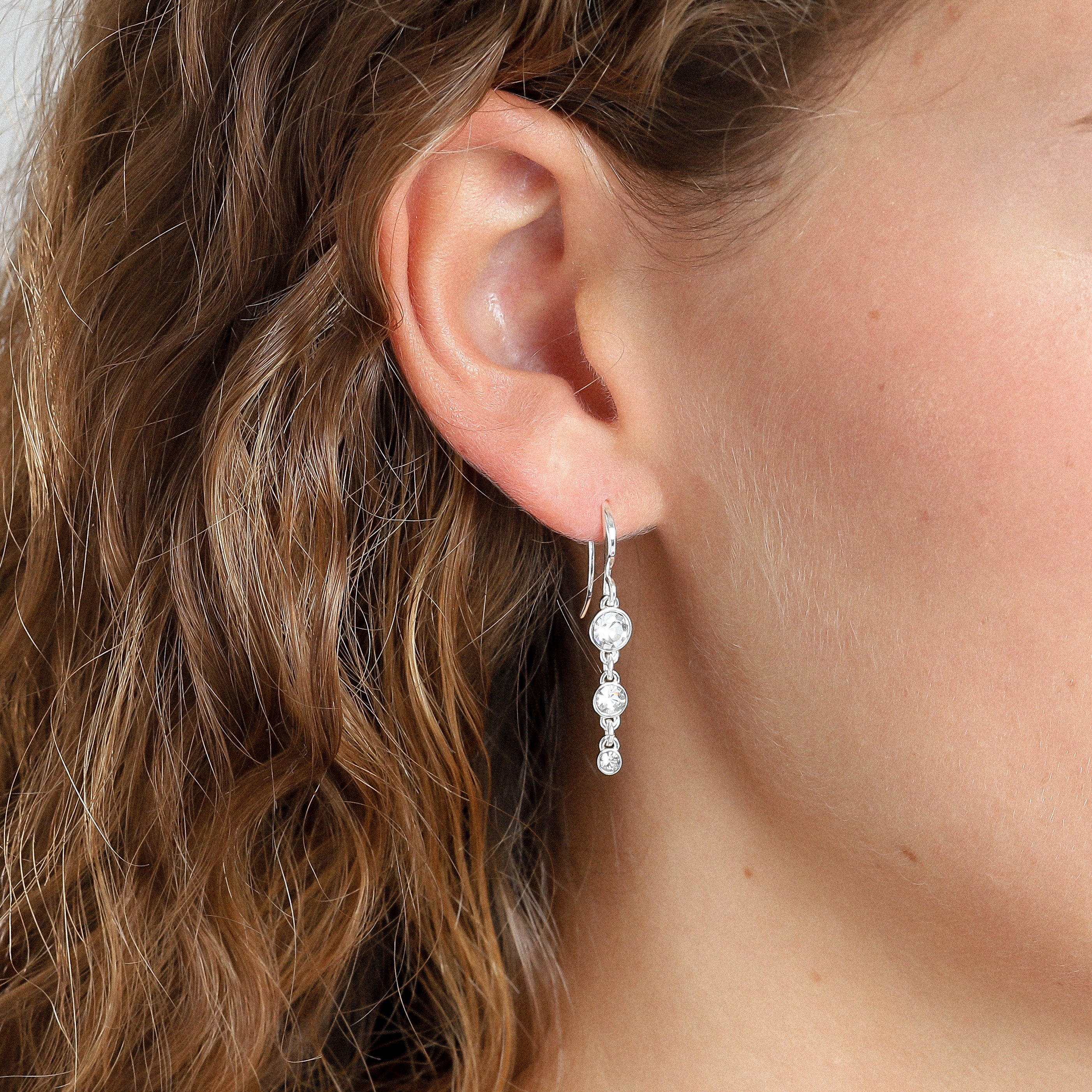 LUCIA crystal earrings silver-plated on a woman's ear, featuring three sparkling crystals in a row, perfect for adding glam to any outfit.