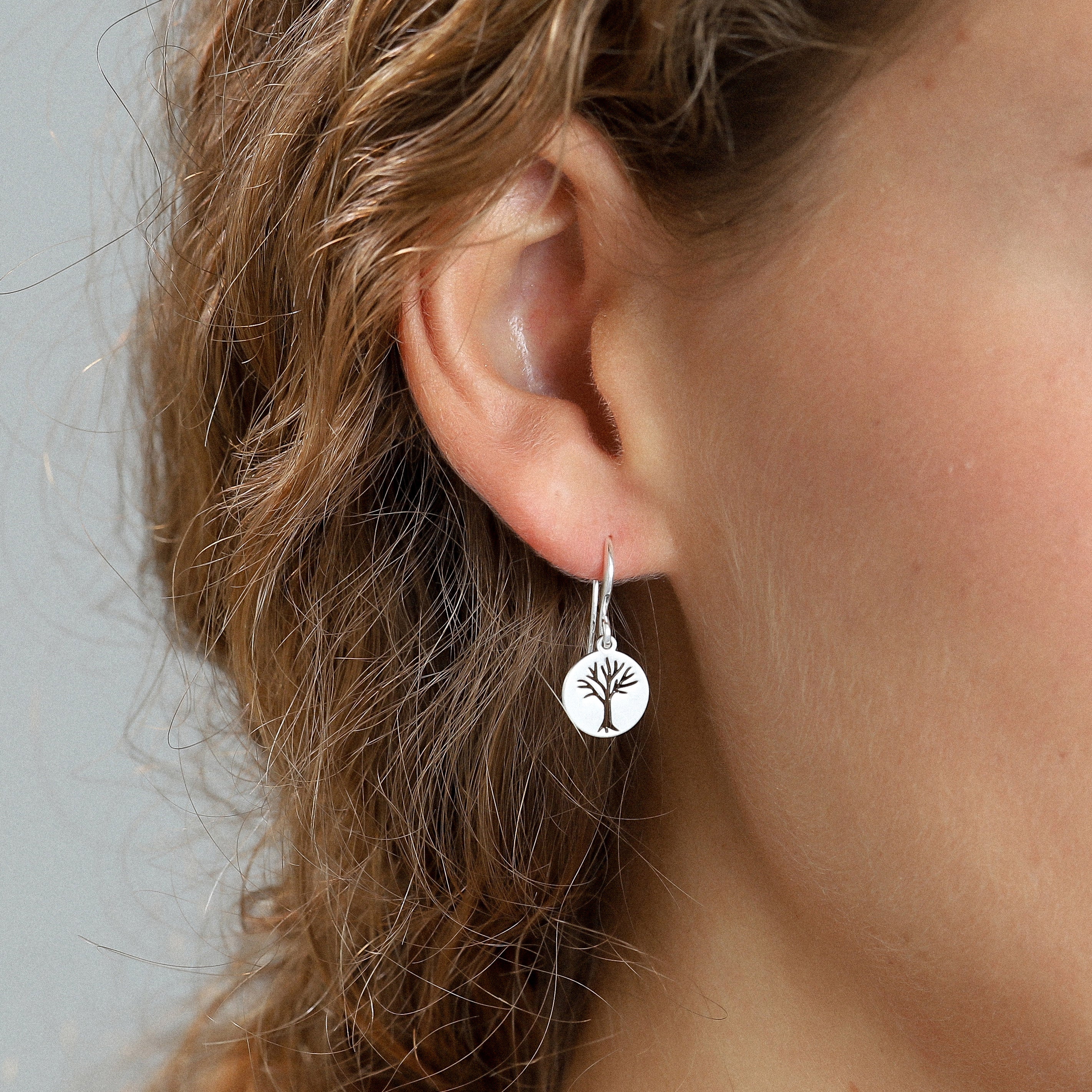 Silver-plated ELIN coin earrings featuring a minimalist tree of life design, worn by a woman, showcasing a modern and stylish accessory trend.