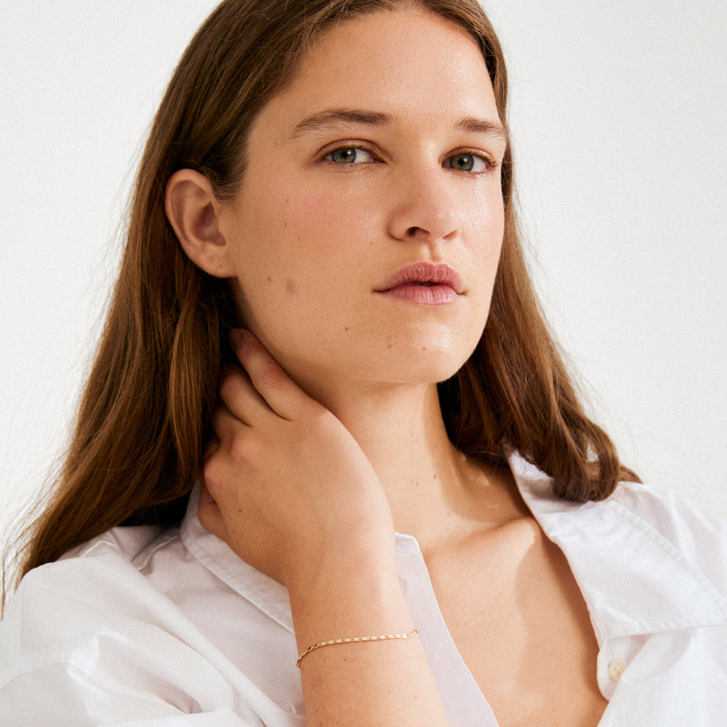 Young woman wearing the PARISA flat link chain bracelet, gold-plated, showcasing its delicate texture and light-reflecting quality on her wrist.