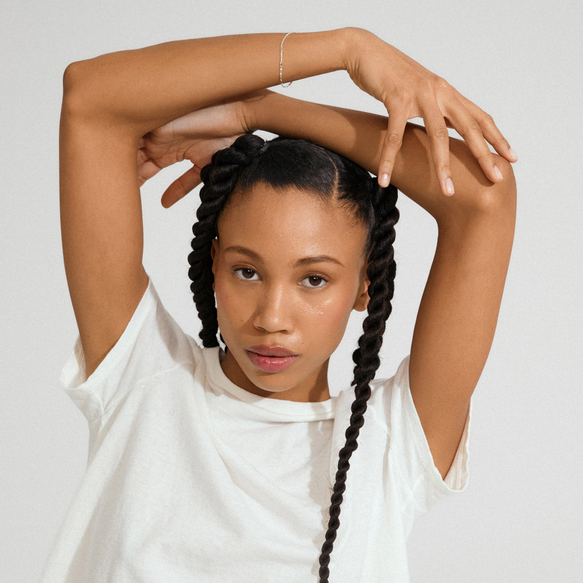 Young woman with braids wearing a PARISA flat link chain bracelet silver-plated, showcasing its delicate texture and reflective elegance against a plain white T-shirt.