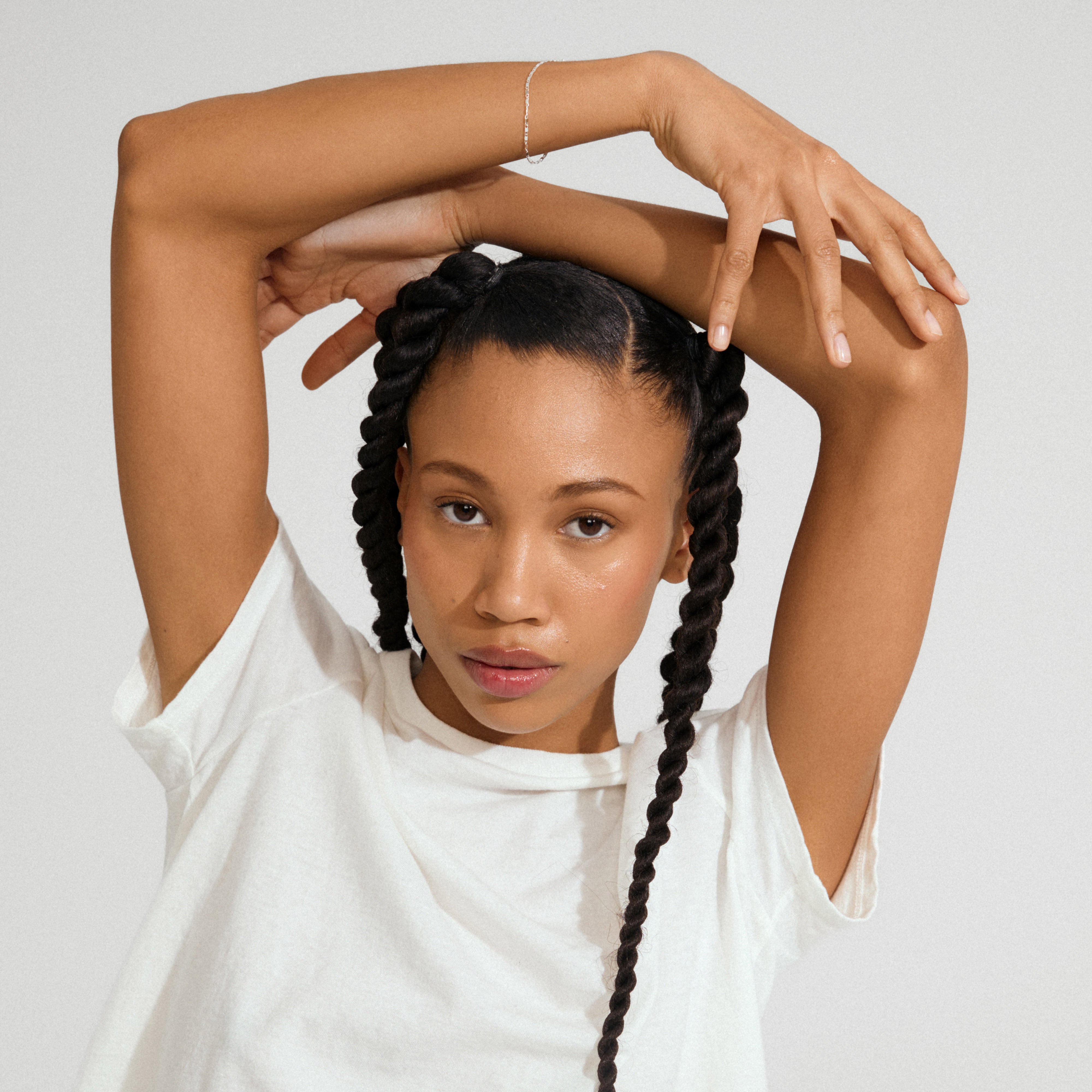 Young woman with braids wearing a PARISA flat link chain bracelet silver-plated, showcasing its delicate texture and reflective elegance against a plain white T-shirt.