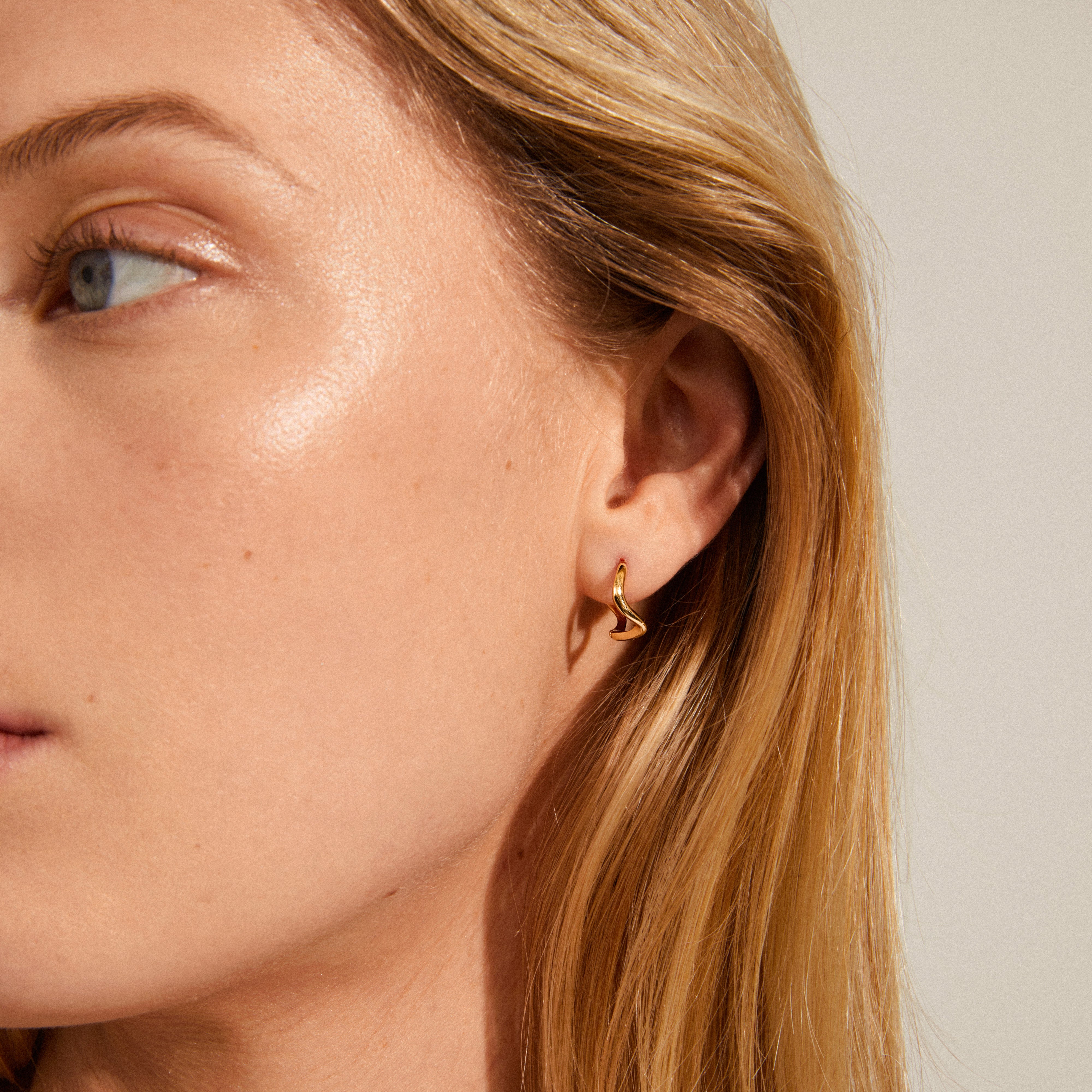Close-up of a woman's ear adorned with ALBERTE organic shape gold-plated hoop earrings, showcasing their wavy, handcrafted design.
