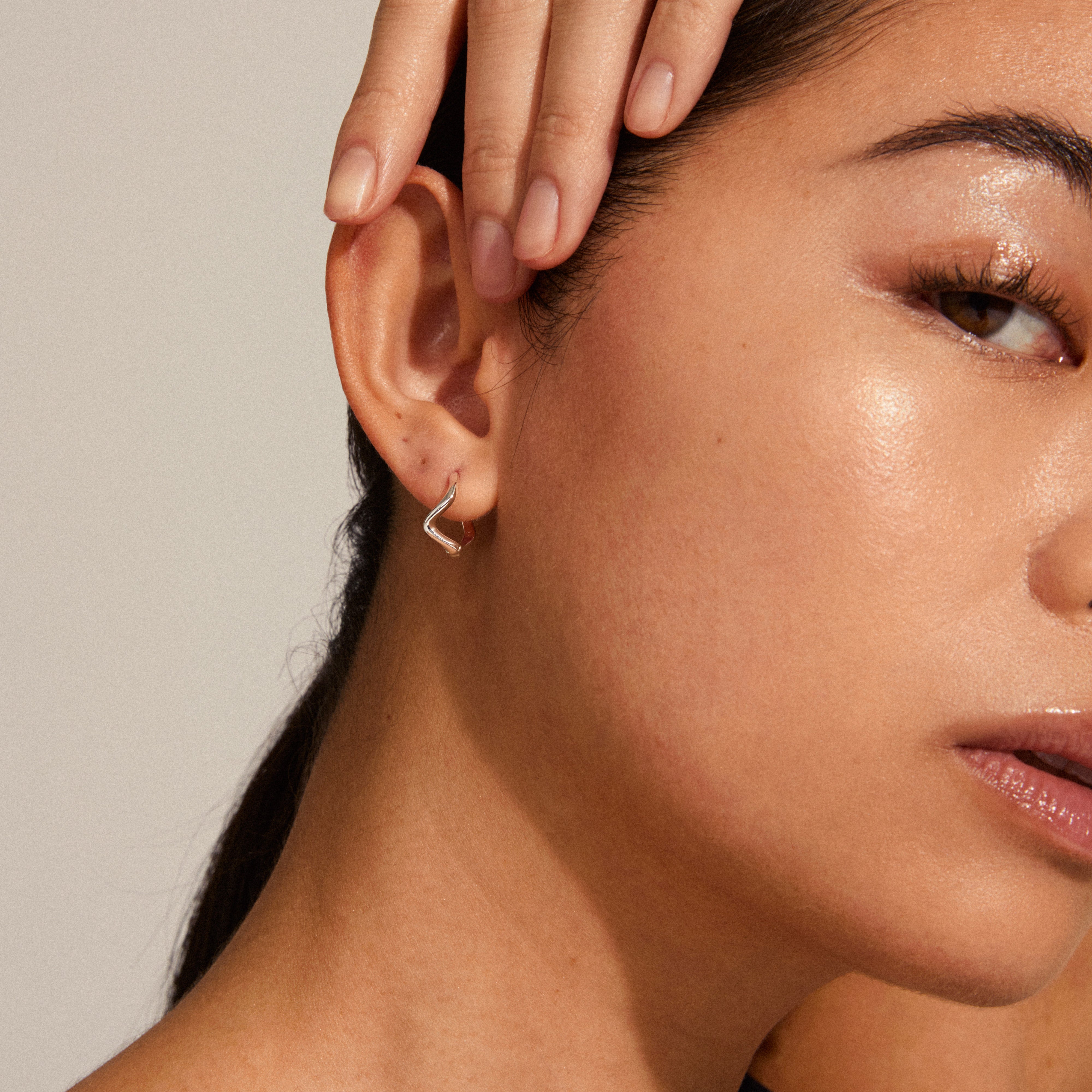 Close-up of a woman wearing Alberte organic shape hoop earrings, silver-plated, showcasing their wavy, nature-inspired design and shiny, handcrafted finish.