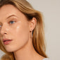 Close-up of a woman wearing Pilgrim's ALBERTE teardrop pendant chain earrings, silver-plated, showcasing their sleek, shiny design and nature-inspired irregular shapes.