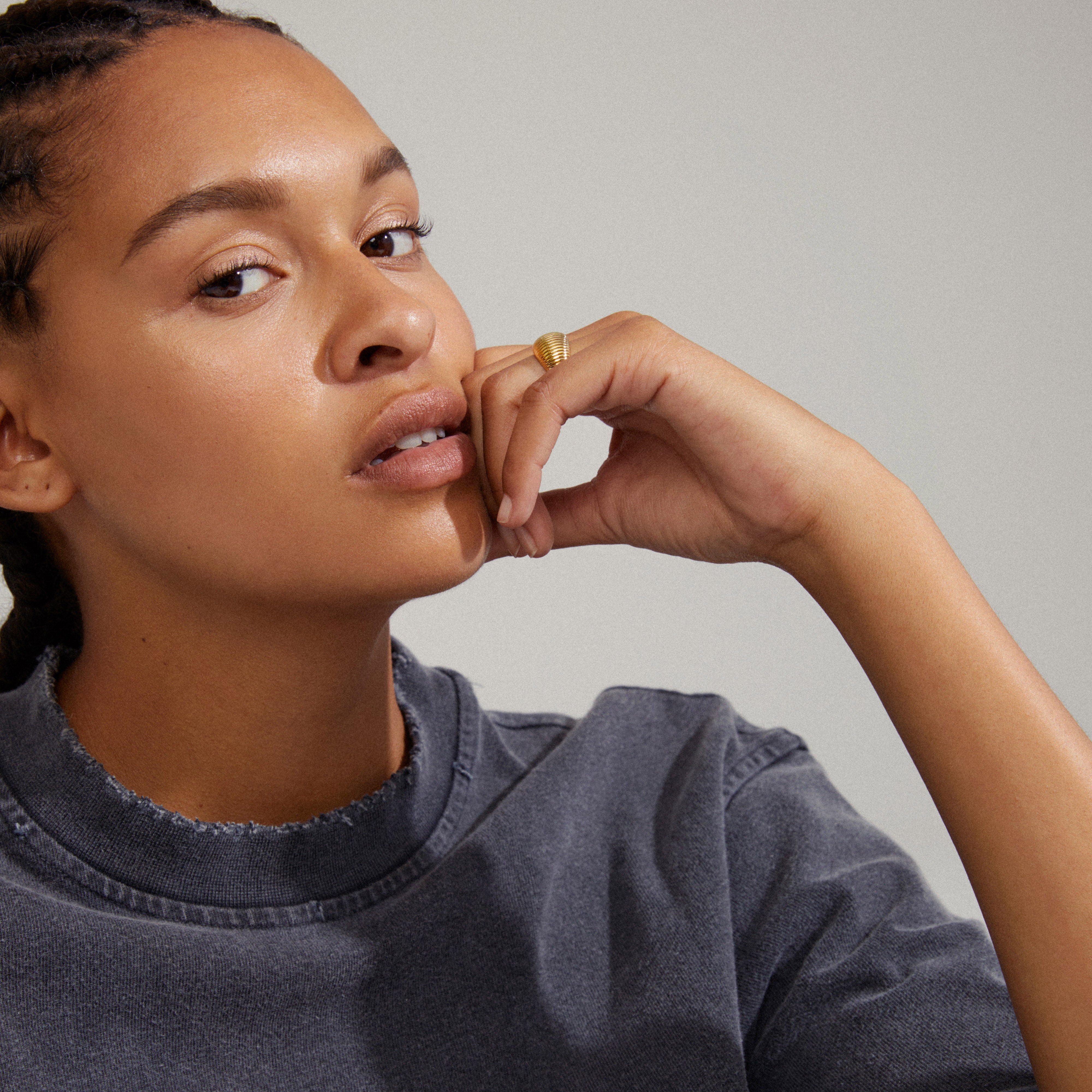 XENA ring gold-plated with groove textures, elegantly held by a woman's hand on her chin, showcasing its classic and unique design.