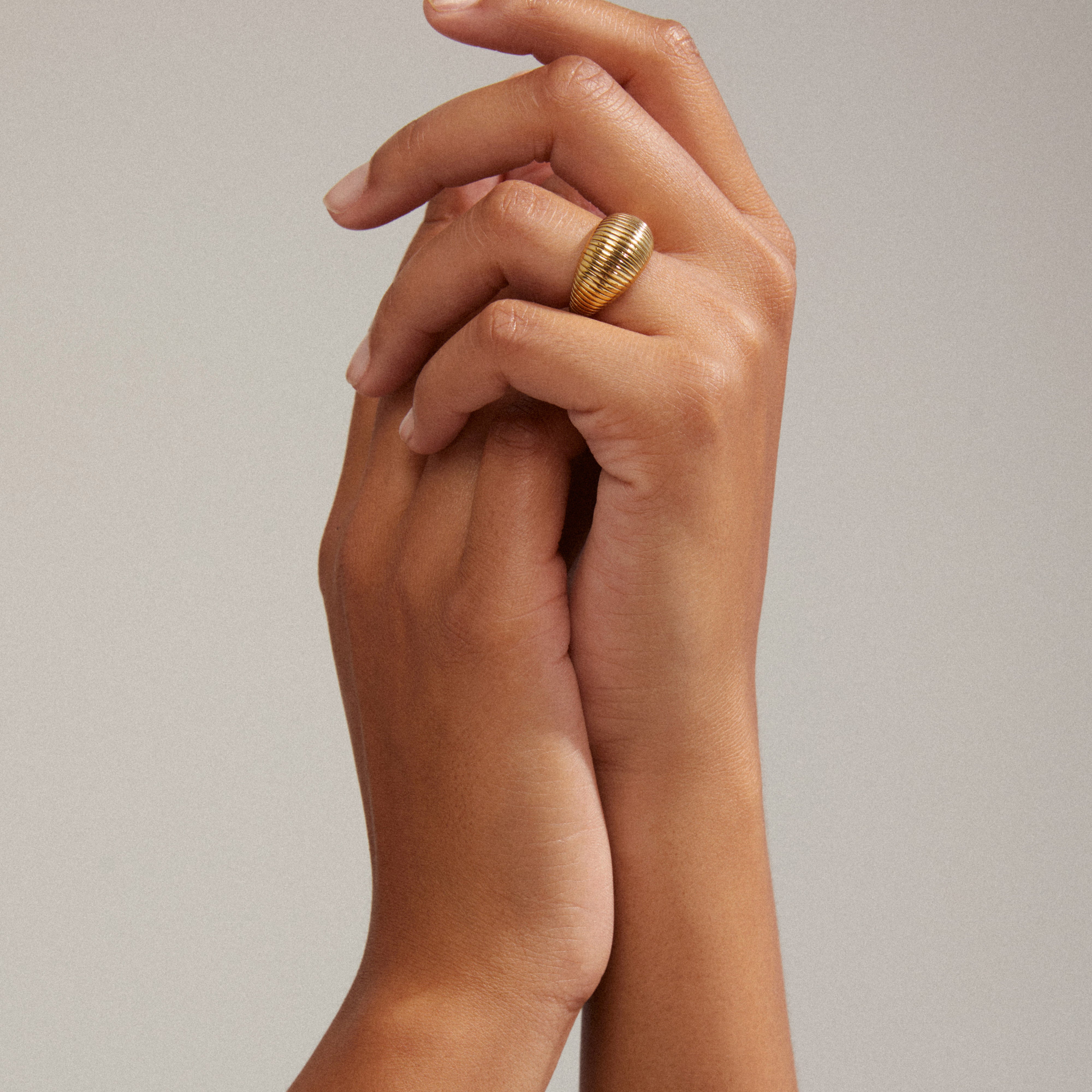 Close-up of hands wearing the XENA ring, gold-plated with groove textures, showcasing its unique, classic design and recycled material craftsmanship.