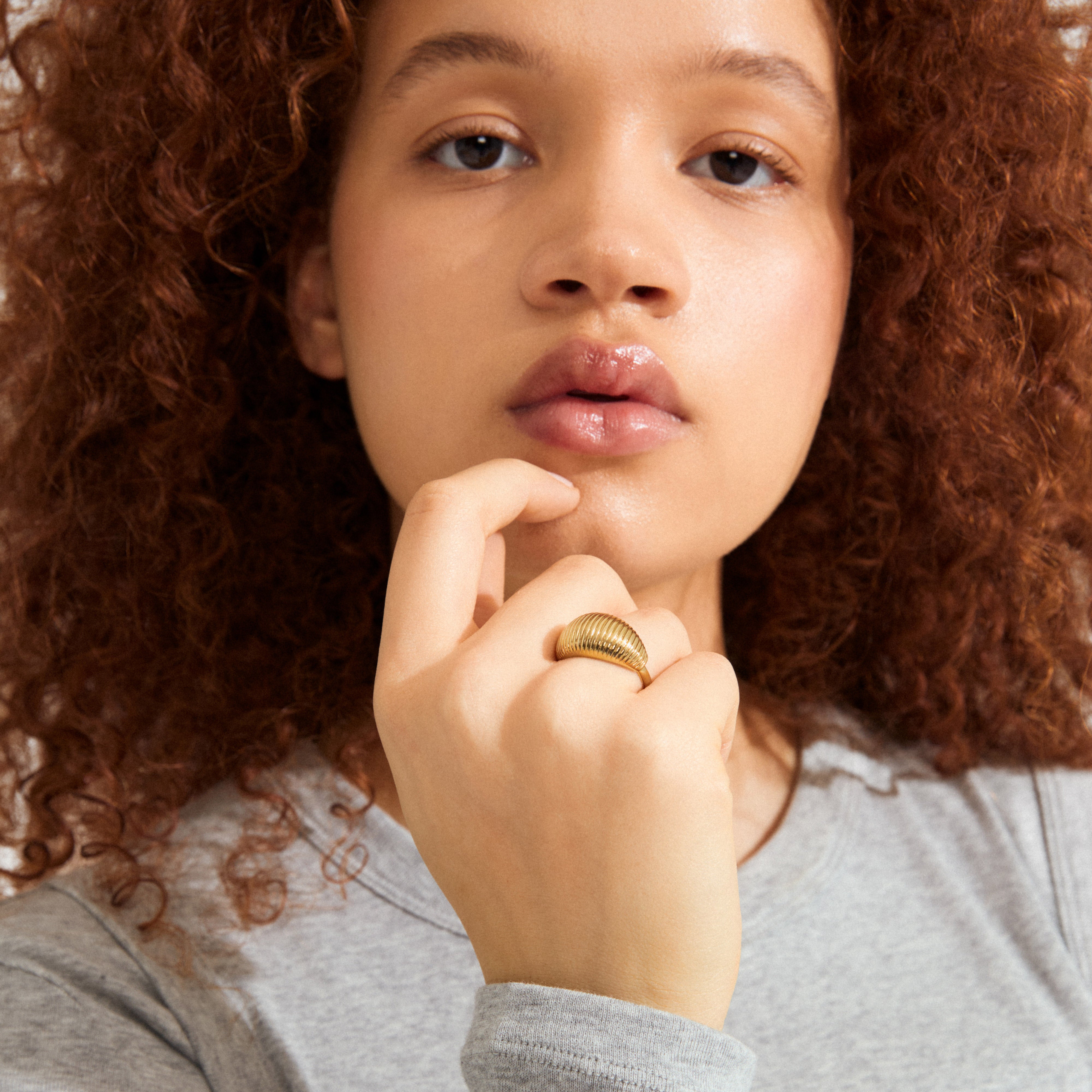 Young person with curly hair, showcasing the XENA ring gold-plated—a chunky, ridged design, exuding character and uniqueness, perfect for an upscale, stylish look.