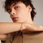 A man models the SOPHIA bangle bracelet gold-plated by Pilgrim, showcasing its classic, shiny design and click lock on his wrist.