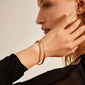 Woman wearing SOPHIA gold-plated bangle bracelet by Pilgrim, showcasing its shiny, classic design with a click lock, accentuating her style.