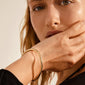 Close-up of a woman wearing the SOPHIA gold-plated bangle bracelet by Pilgrim, showcasing its elegant, shiny surface and classic design.