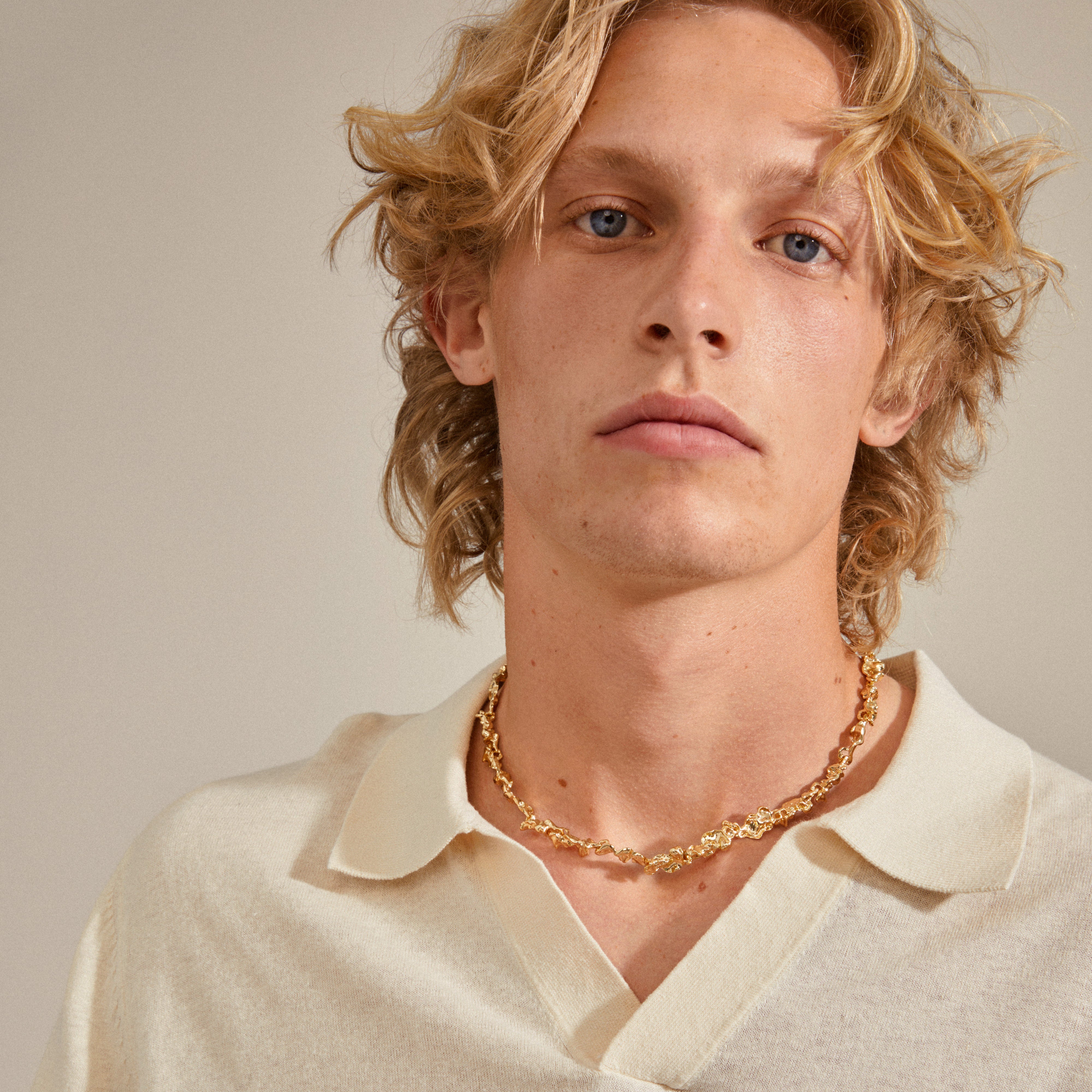 Blonde man wearing Pilgrim's RAELYNN gold-plated necklace with organic, handcrafted links, highlighting Scandinavian design and style.