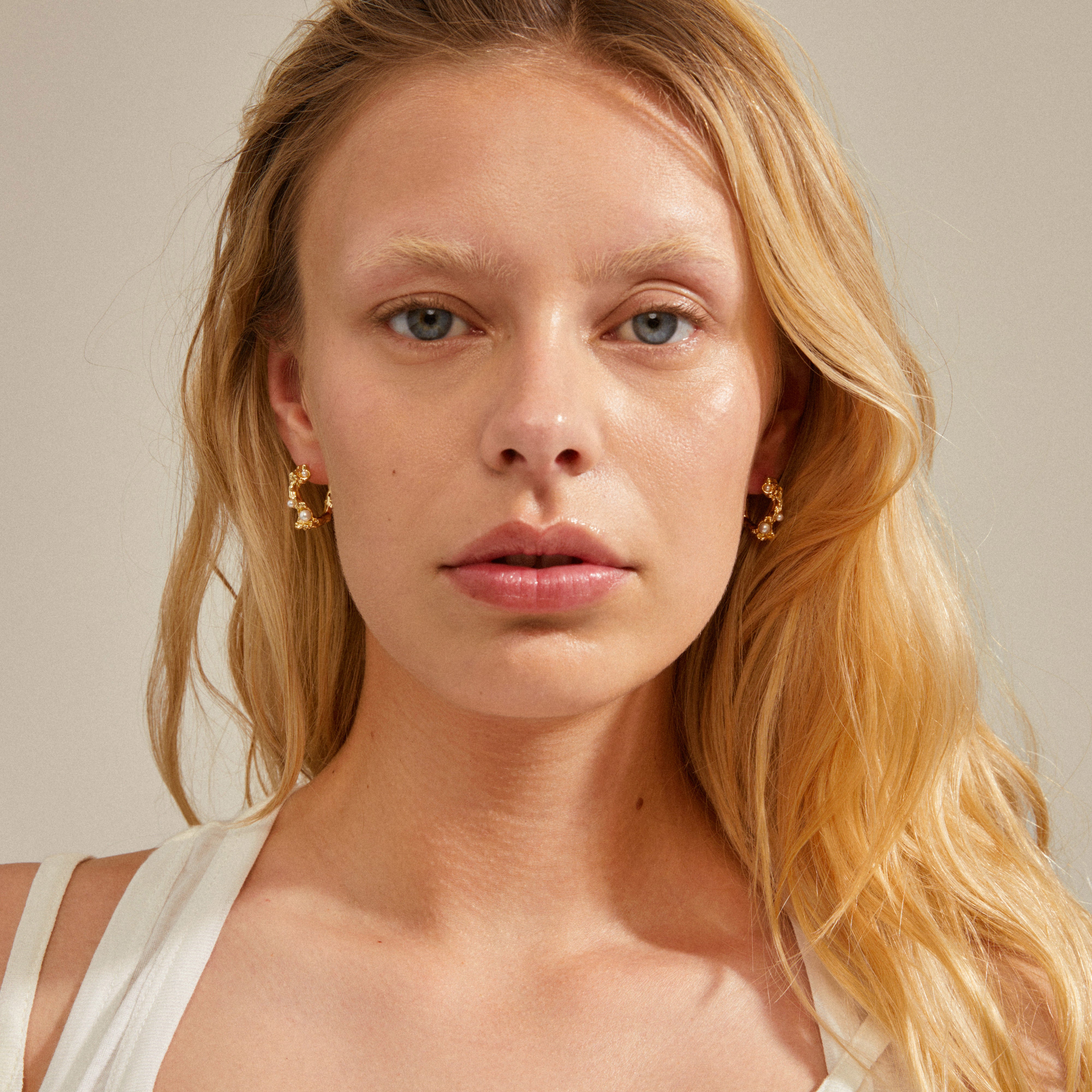 RAELYNN earrings gold-plated; close-up of a woman wearing organically shaped hoops with small white beads, exuding a cool, luxurious vibe.