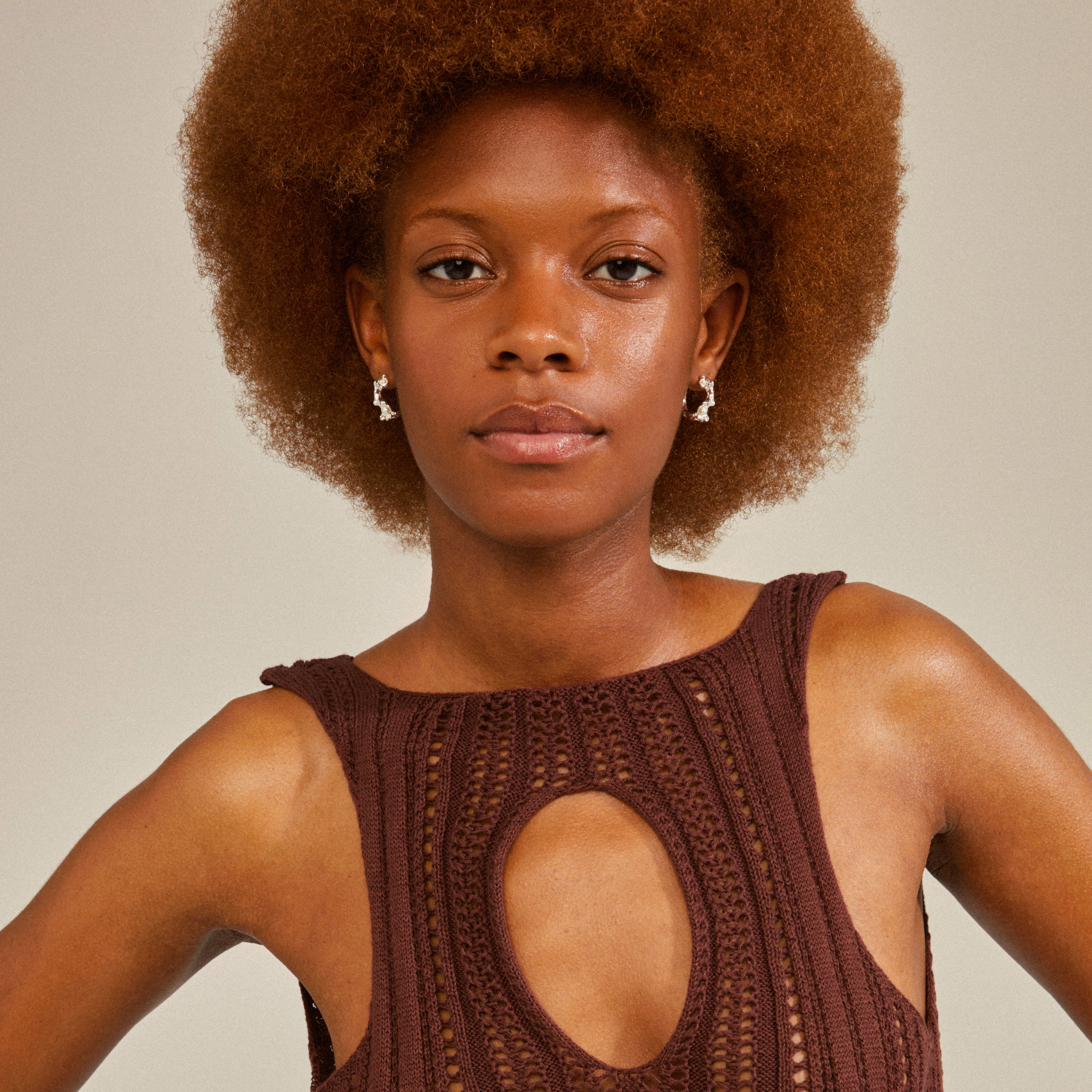 A woman with curly hair wears RAELYNN silver-plated hoops featuring an organic texture and white beads, embodying playful energy and eco-friendly design.