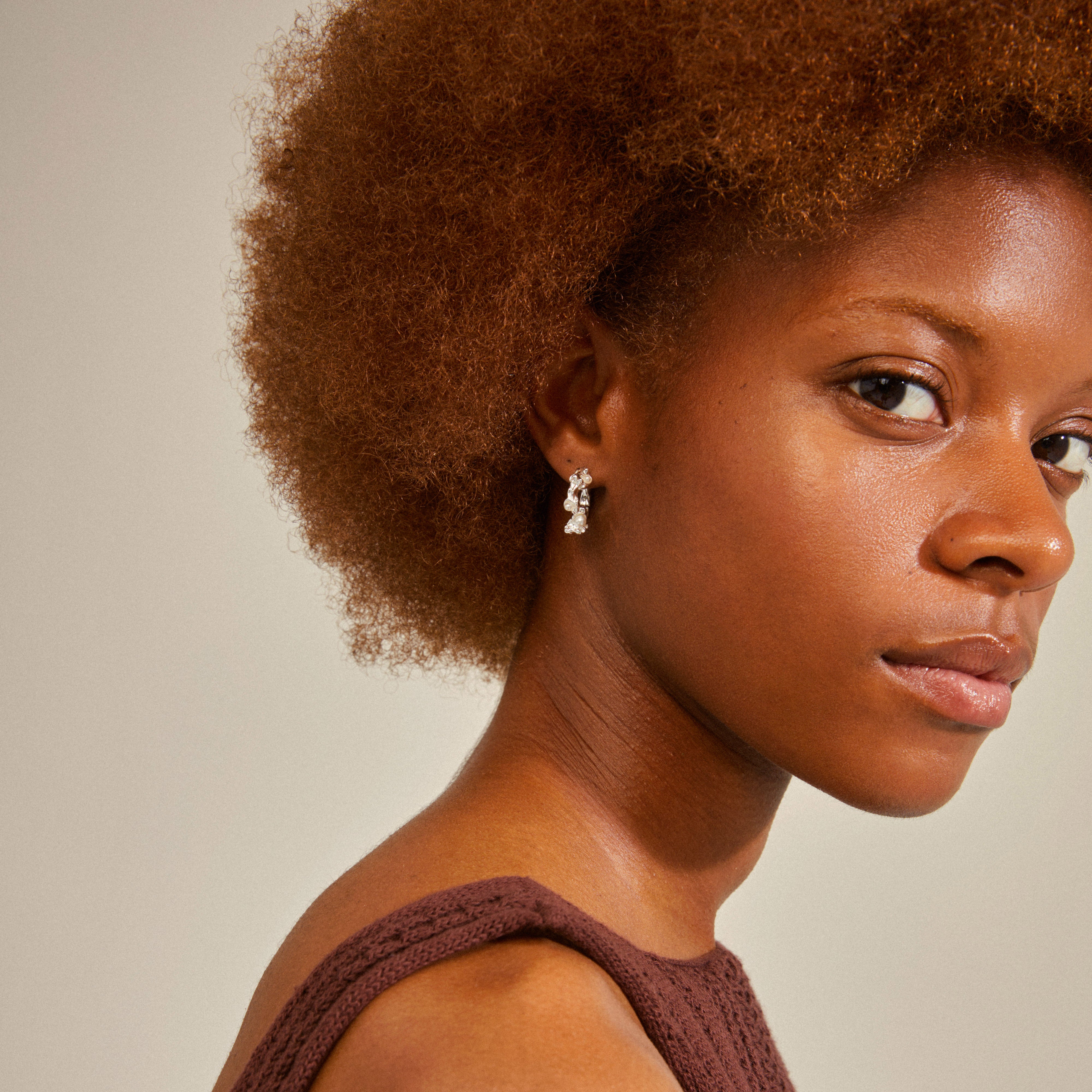 Silver-plated RAELYNN hoops with organic texture and small white beads, worn by a woman with curly hair, showcasing playful and summery vibes.