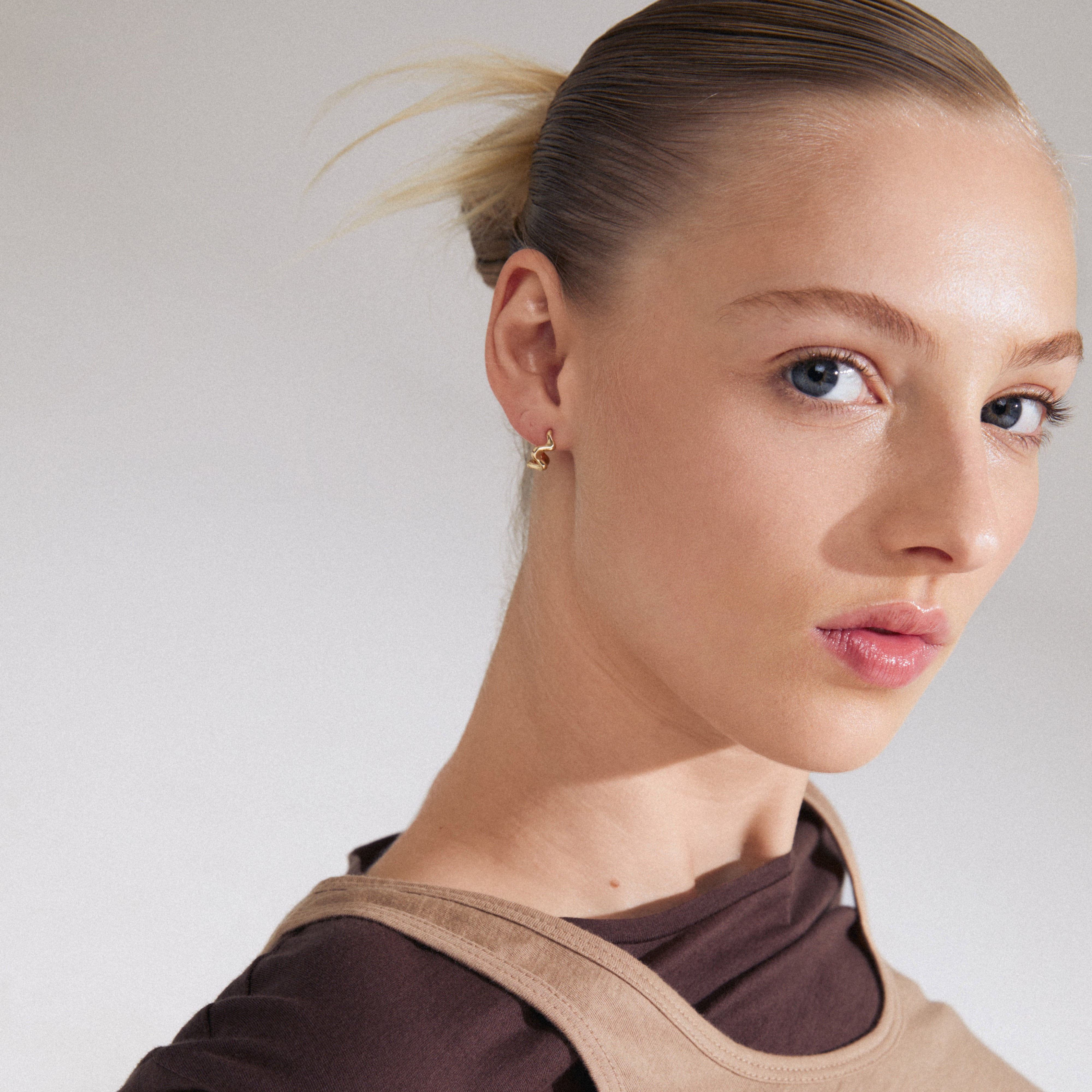 Close-up of a woman wearing PENELOPE gold-plated earrings from Pilgrim, showcasing their curvy, wavy design and easy click clasp.