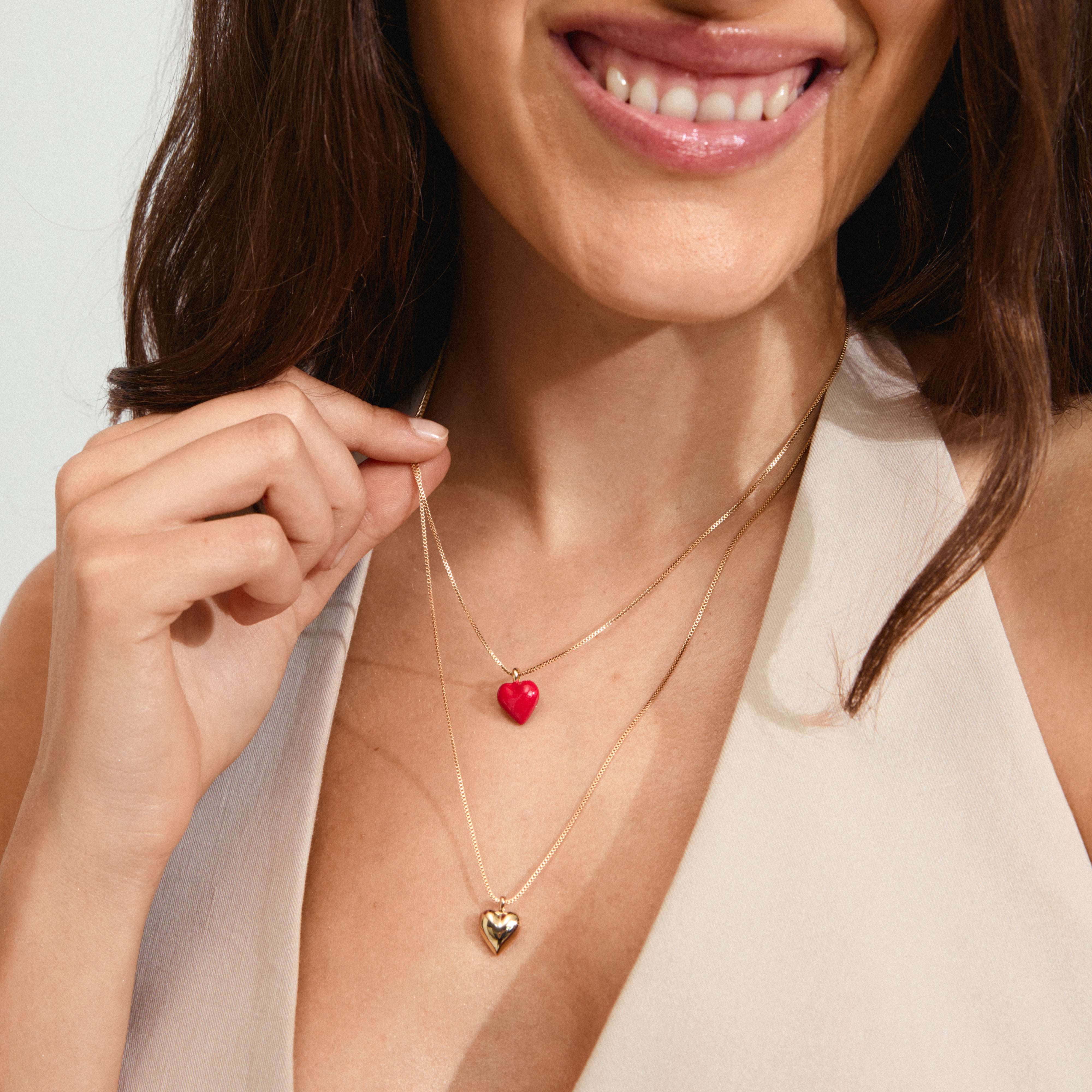 Woman smiling, showcasing the MAEVE necklace, a 2-in-1 gold-plated set from Pilgrim, featuring a heart pendant and a slim box chain.