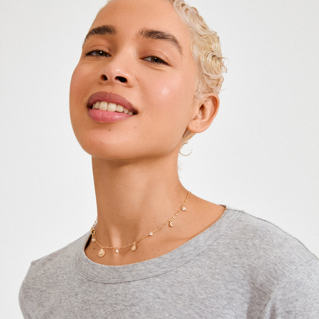 Close-up of a young person wearing the gold-plated MYLAN necklace by Pilgrim, featuring sun, moon, and heart charms on a delicate chain.