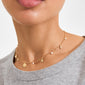 Close-up of MYLAN necklace, gold-plated with sunburst, crescent moon charms, and tiny pearls, worn over a light grey top.