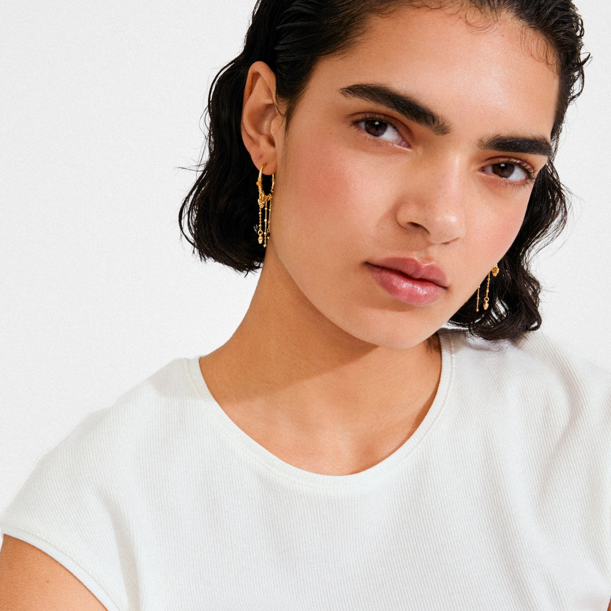 Young woman wearing MYLAN gold-plated earrings with delicate charms, showcasing Pilgrim's blend of timeless and trendy Scandinavian jewellery style.