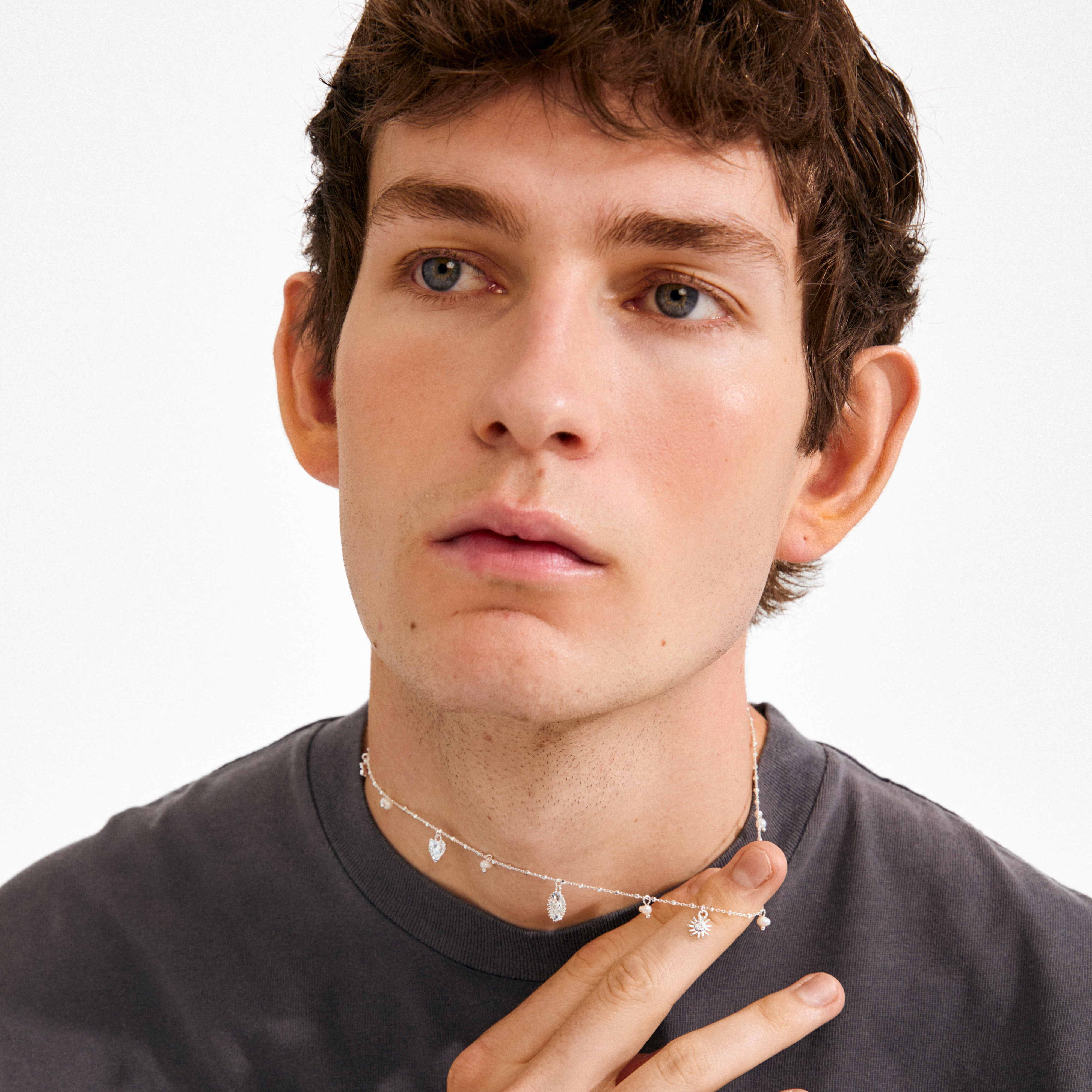 Young man holding Pilgrim's silver-plated MYLAN necklace, featuring symbolic charms like sun, moon, and heart, crafted with recycled materials for a mystical, whimsical vibe.