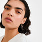Close-up of MYLAN earrings silver-plated, featuring delicate chains and charms, worn by a young person with sleek hair and a white top.