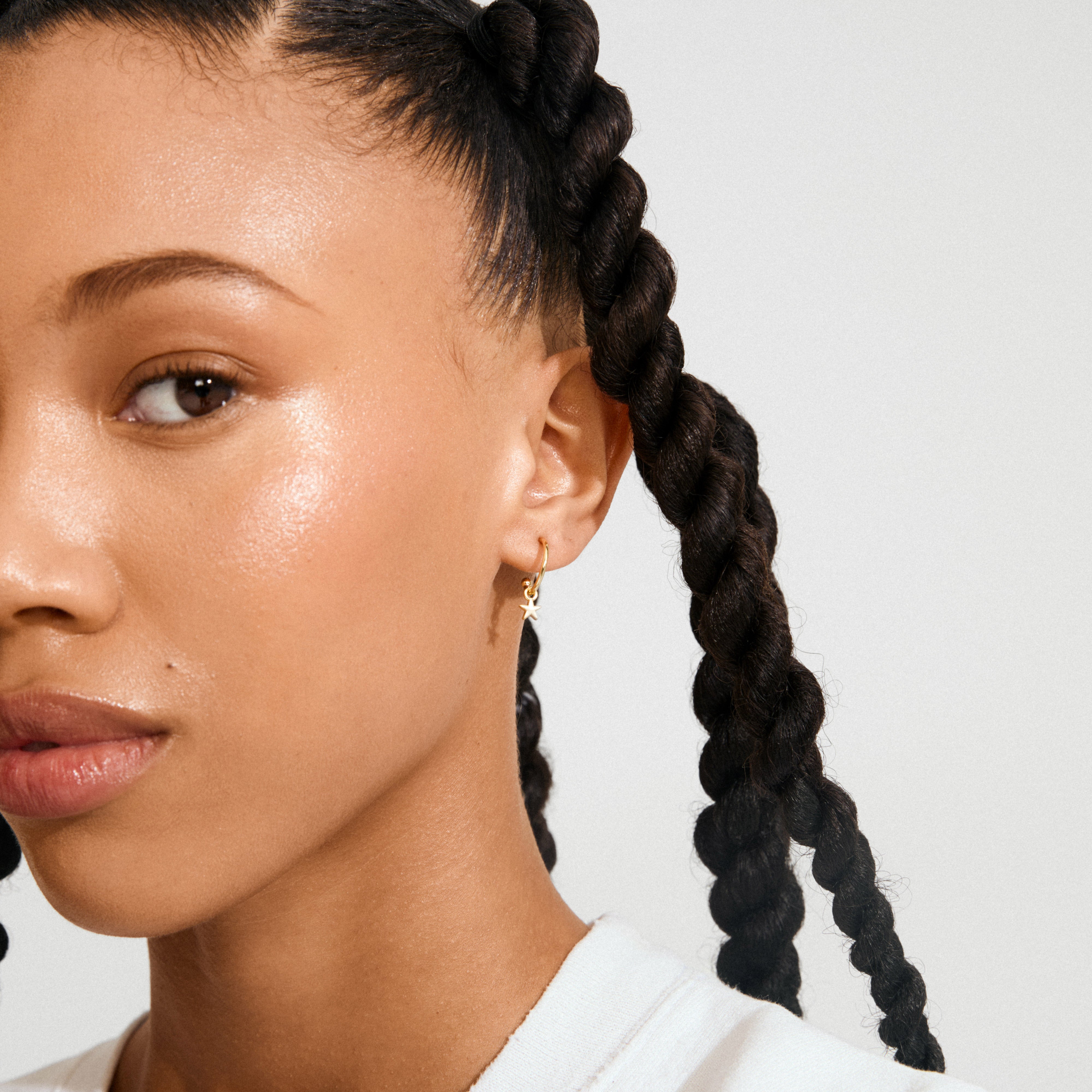 Young person wearing AVA star hoop earrings gold-plated, featuring small star charms, highlighting a sweet and feminine vibe against smooth skin and thick braids.