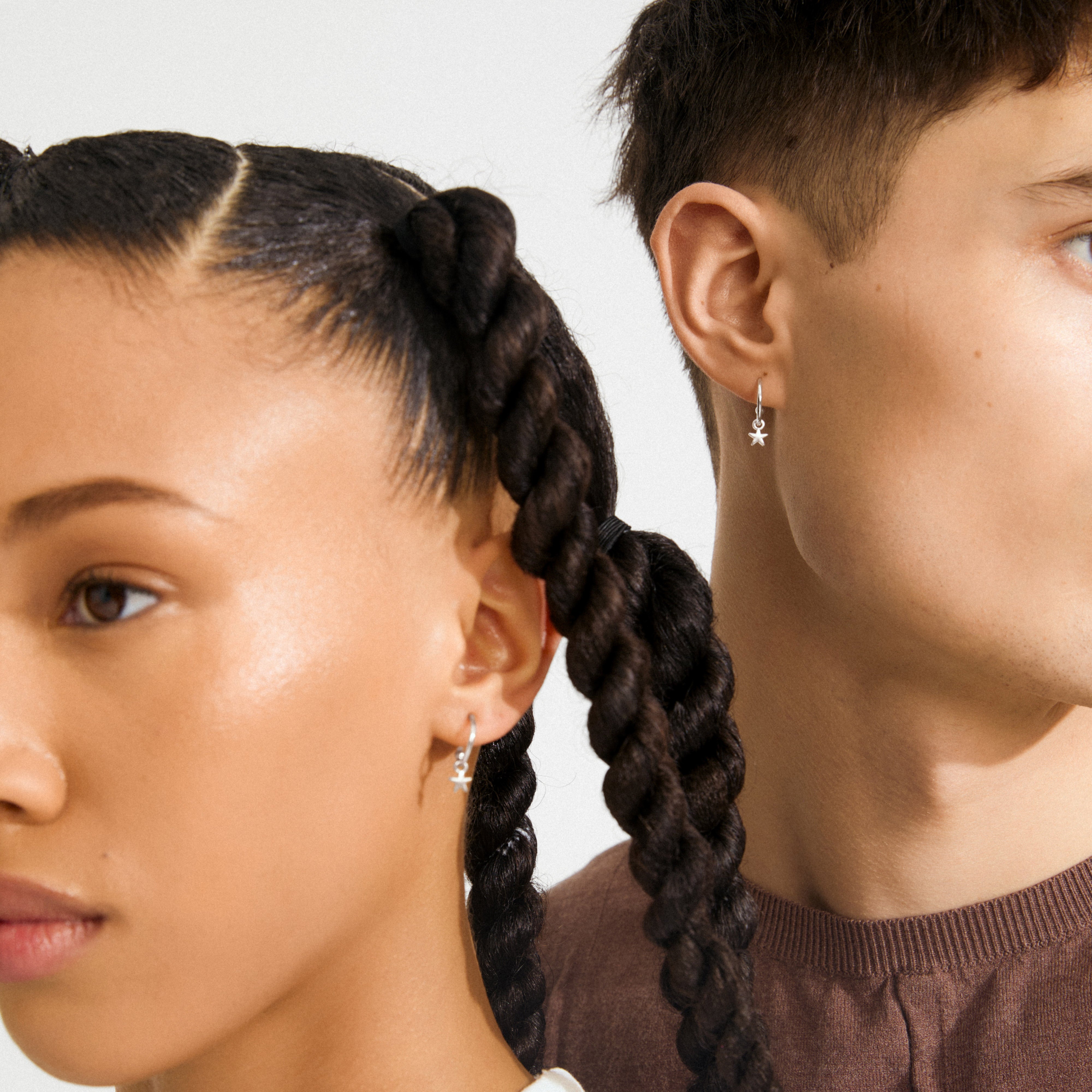 Two individuals in profile wear AVA star hoop earrings, silver-plated with tiny star charms, showcasing Pilgrim's blend of timeless and trendy Danish design.