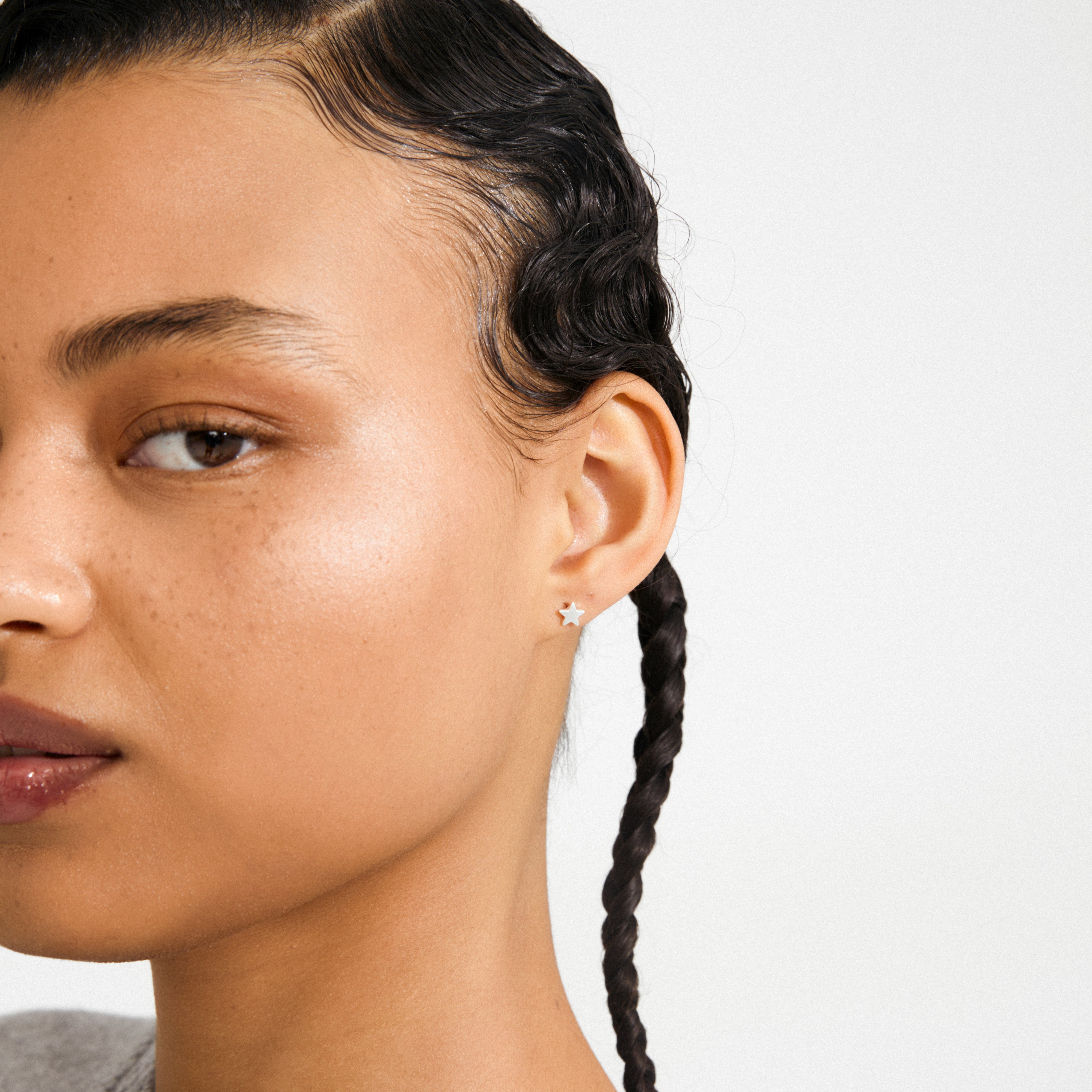 Close-up of a person wearing AVA star earrings, silver-plated with a velvet-matt texture, showcased against slicked-down braids in a minimalist setting.