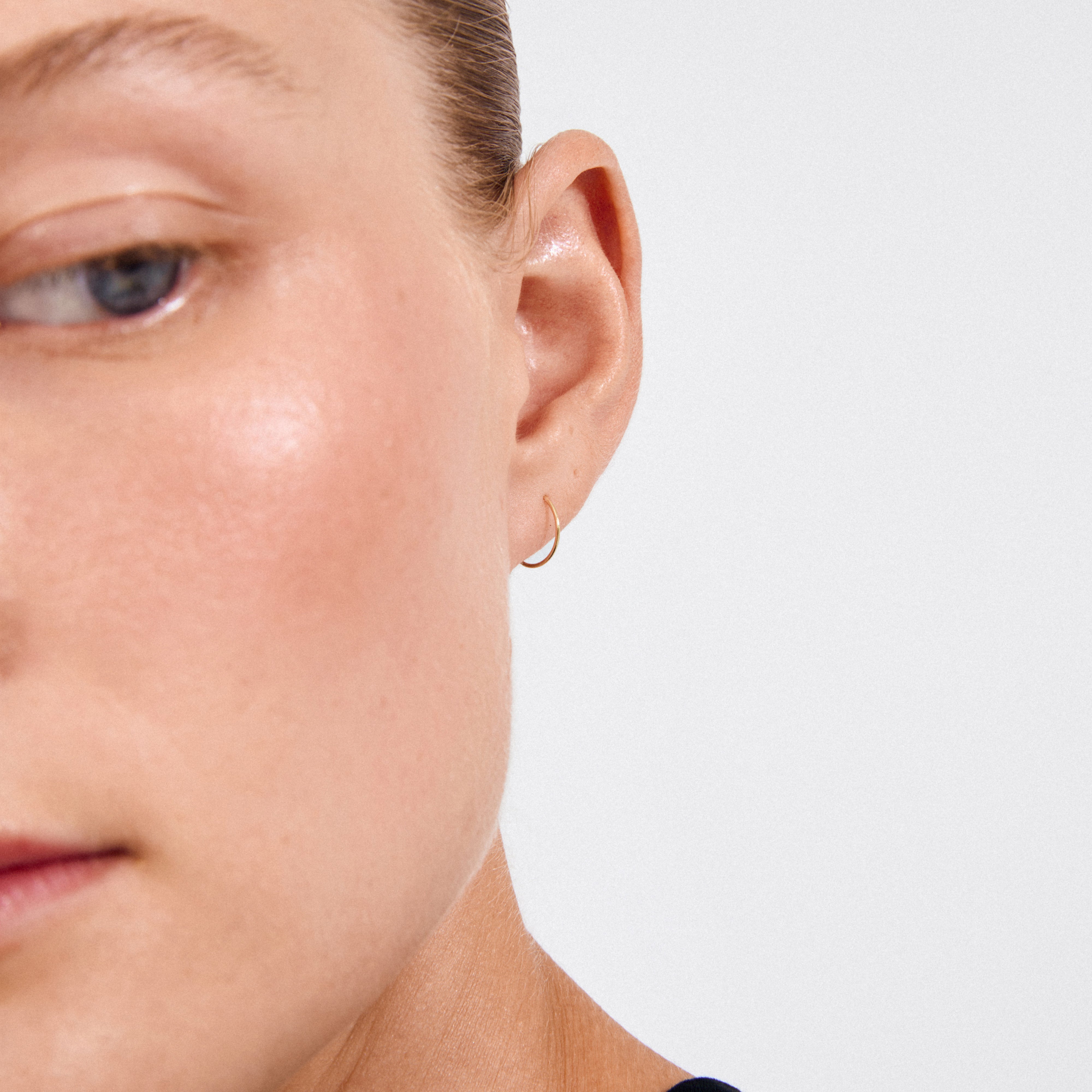 Close-up of a person's ear wearing RAQUEL mini hoop earrings, gold-plated, showcasing their elegant design and craftsmanship from recycled materials for versatile styling.