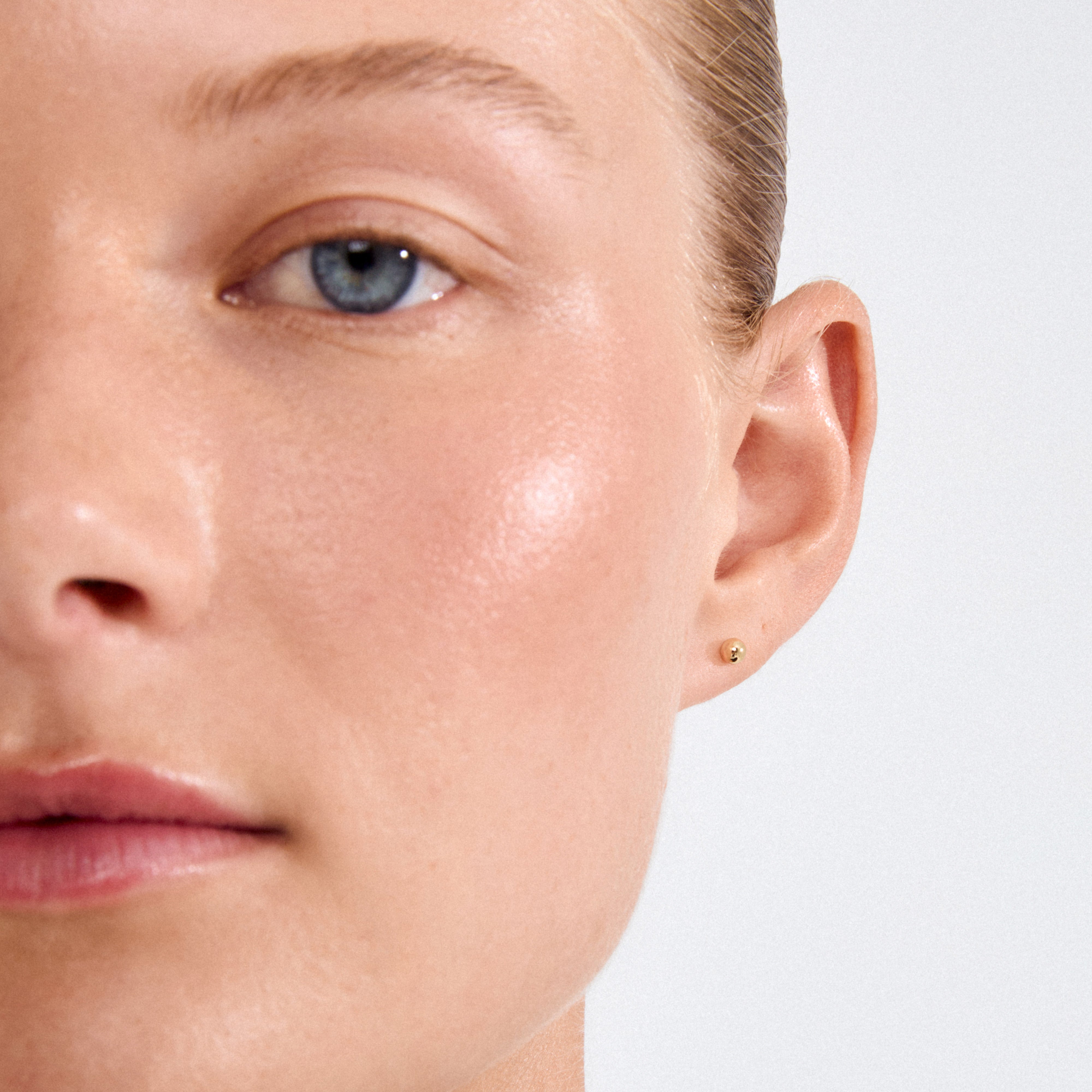 Close-up of a person wearing MOLLY earstuds gold-plated, featuring a tiny pearl, showcasing Pilgrim's Scandi minimalist design aesthetic.