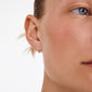 Close-up of a left ear featuring RAQUEL mini hoop earrings, silver-plated, showcasing smooth skin and light hair. Timeless design, crafted from 99% recycled materials.