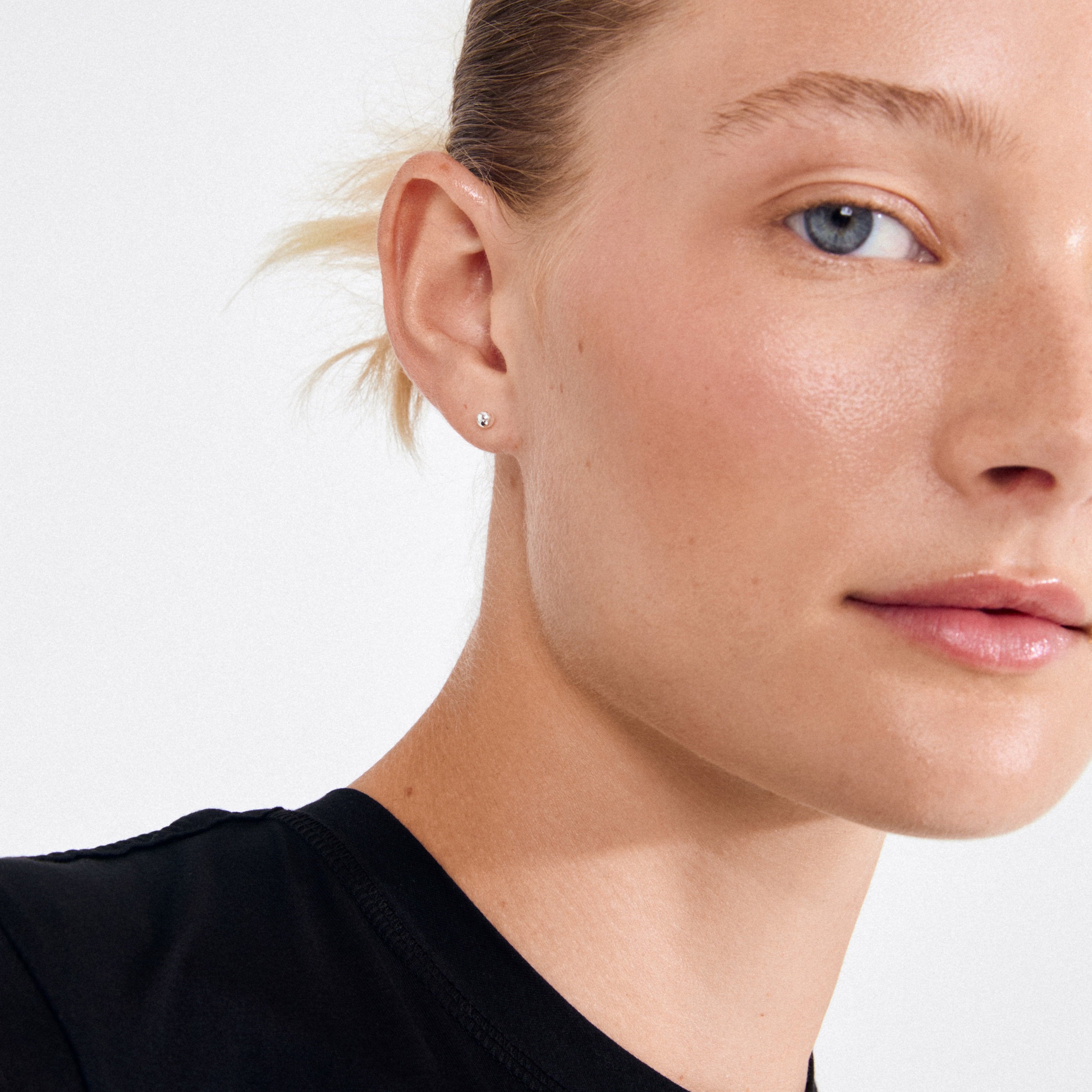 Close-up of a woman's ear wearing MOLLY earrings, silver-plated studs with tiny pearls, showcasing Pilgrim's Scandi minimalism and sustainable craftsmanship.