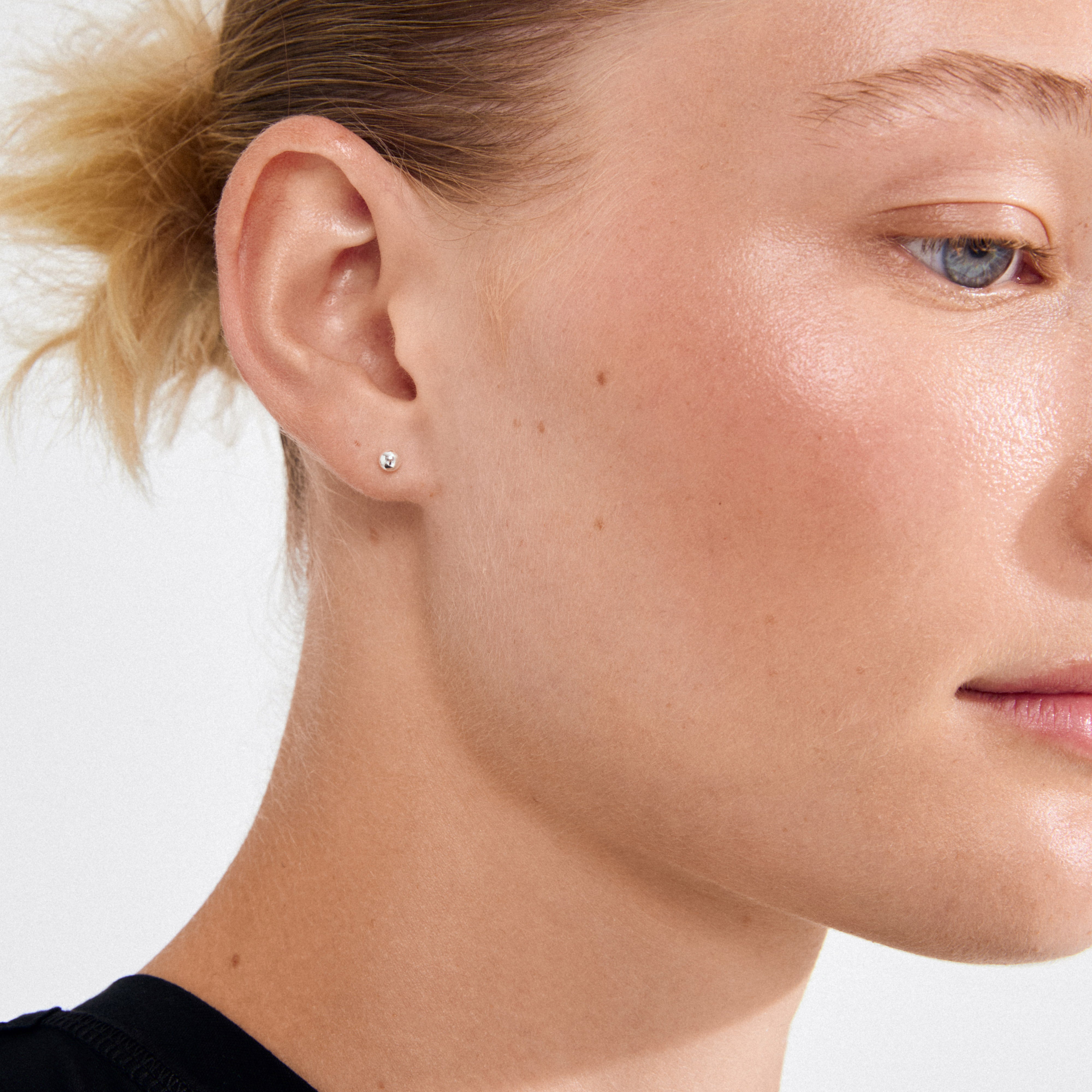 Profile close-up of a fair-skinned individual wearing a black top, showcasing Pilgrim's MOLLY silver-plated stud earring with tiny pearls, embodying Scandi minimalism.