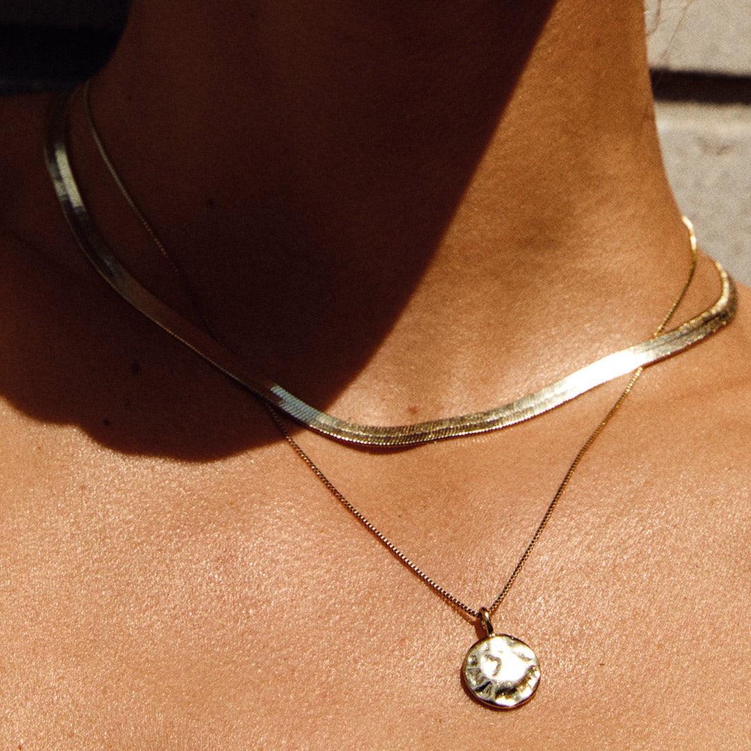 NOREEN flat snakechain necklace gold-plated, featuring polished serpent design with intricate flat links, elegantly draped on a neck, showcasing its stylish and exotic appeal.