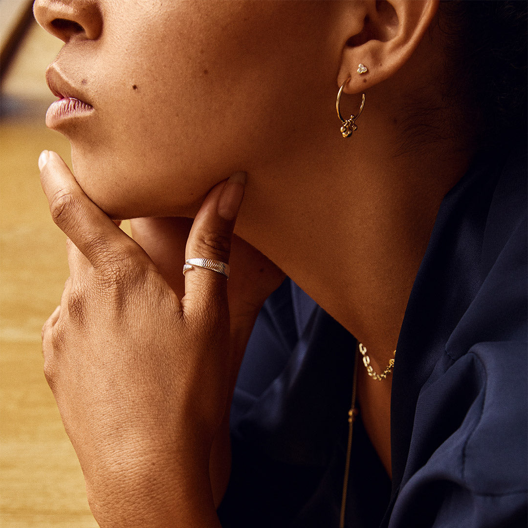 NOREEN ring silver-plated features a broad band with a textured, industrial-inspired pattern, visible on a woman's hand touching her chin.