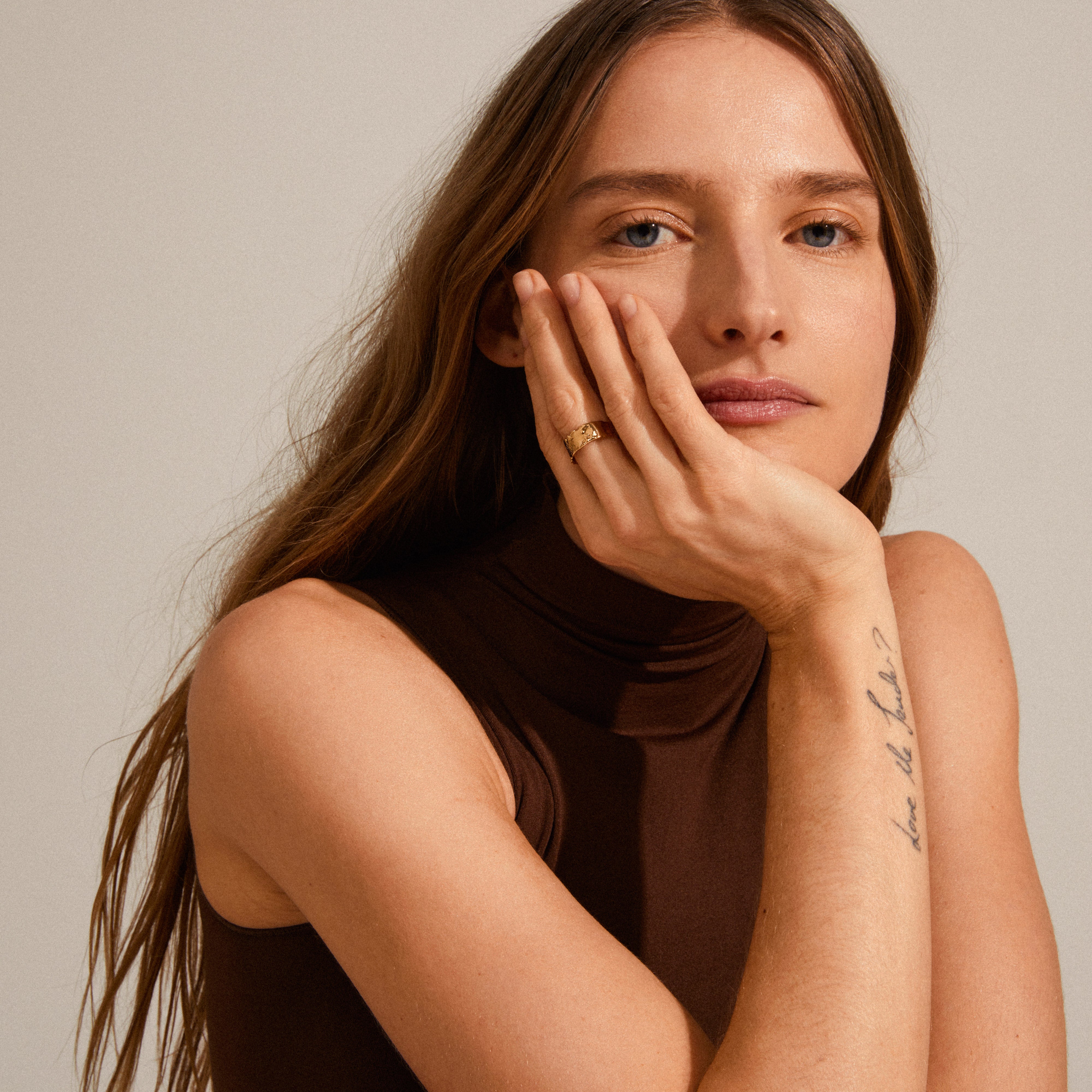 Close-up of a woman wearing the BATHILDA rustic gold-plated ring with a hammered texture, elegantly resting her hand on her face.