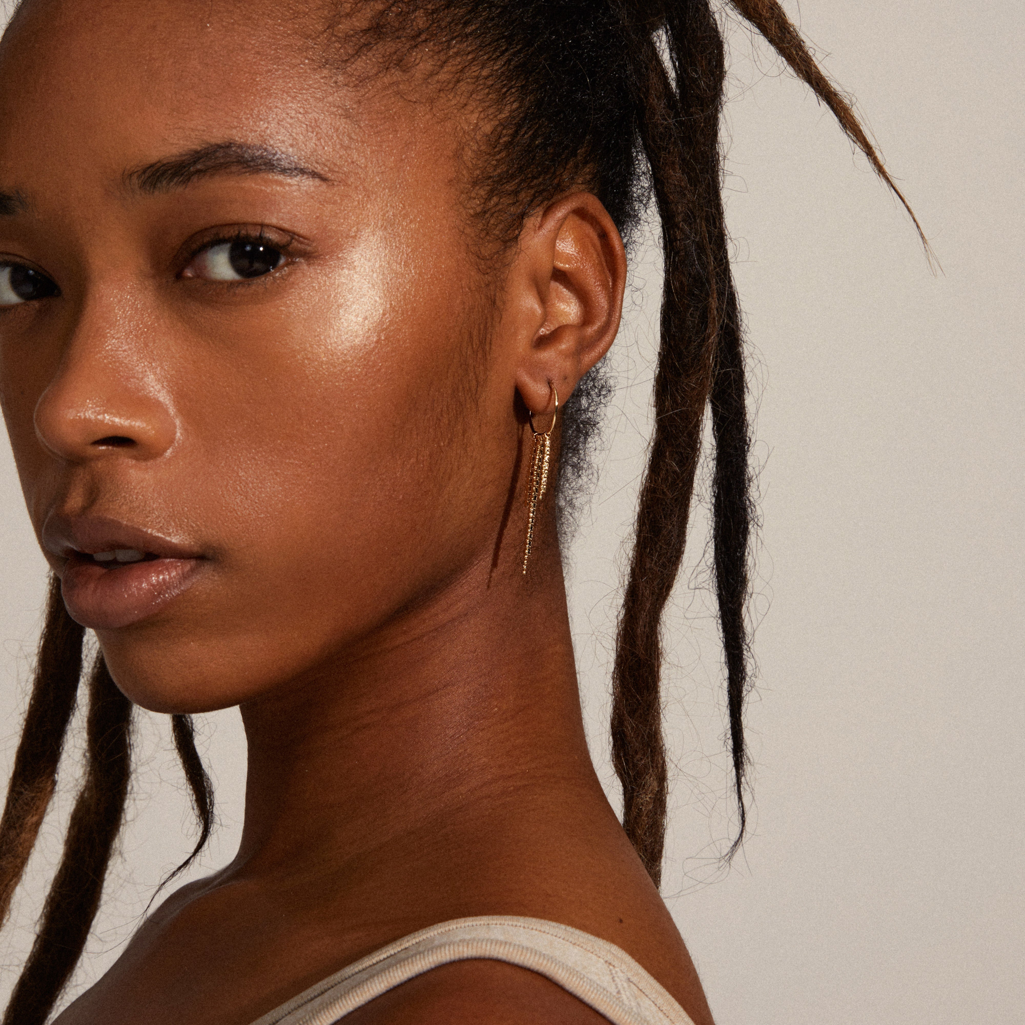 Woman with dreadlocks wearing MAJA crystal waterfall hoop earrings, featuring asymmetrical gold pendants with Preciosa crystals, adding a stylish edge.