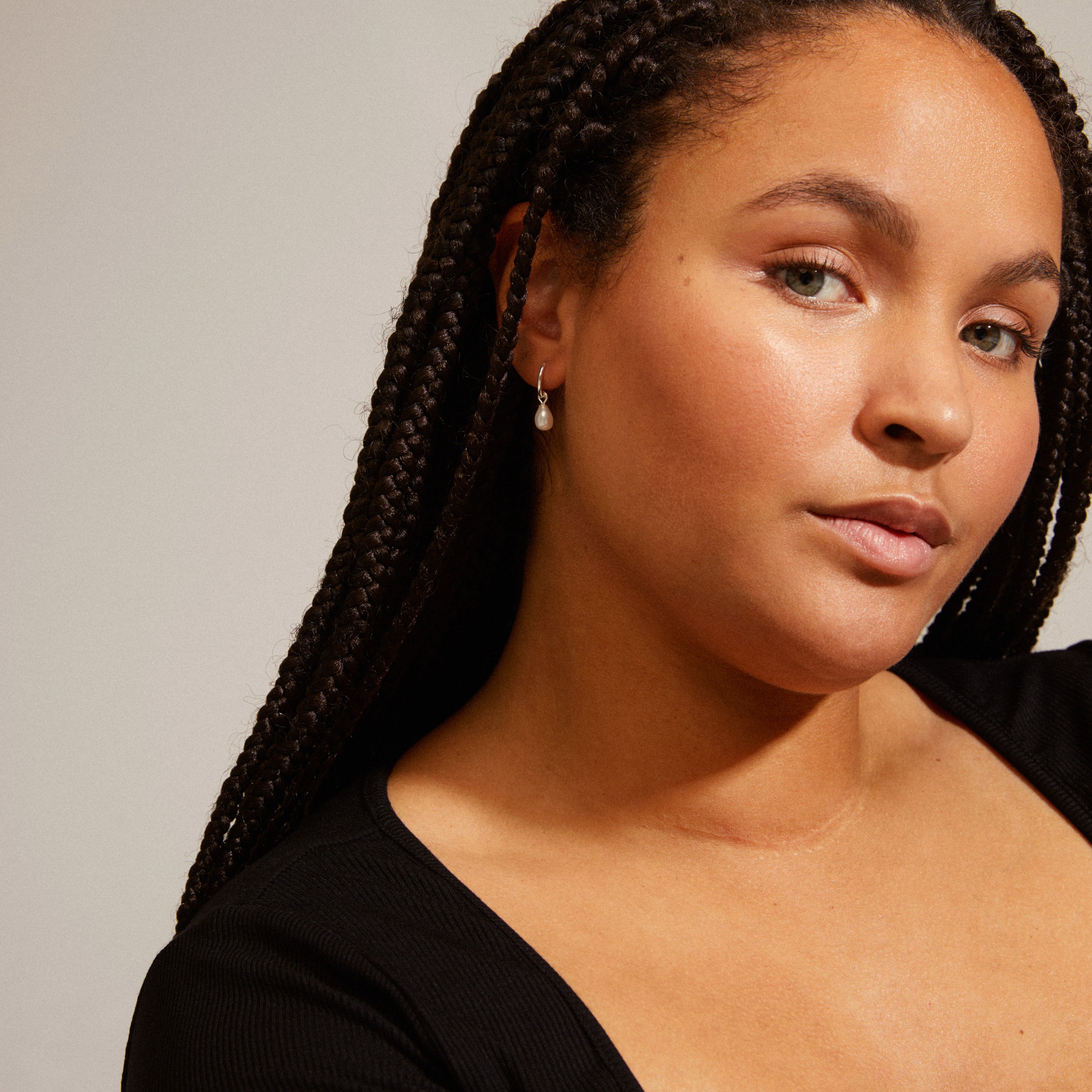 Woman wearing BERTHE pearl hoop earrings, silver-plated with white freshwater pearl pendants, highlighting natural elegance and simplicity.