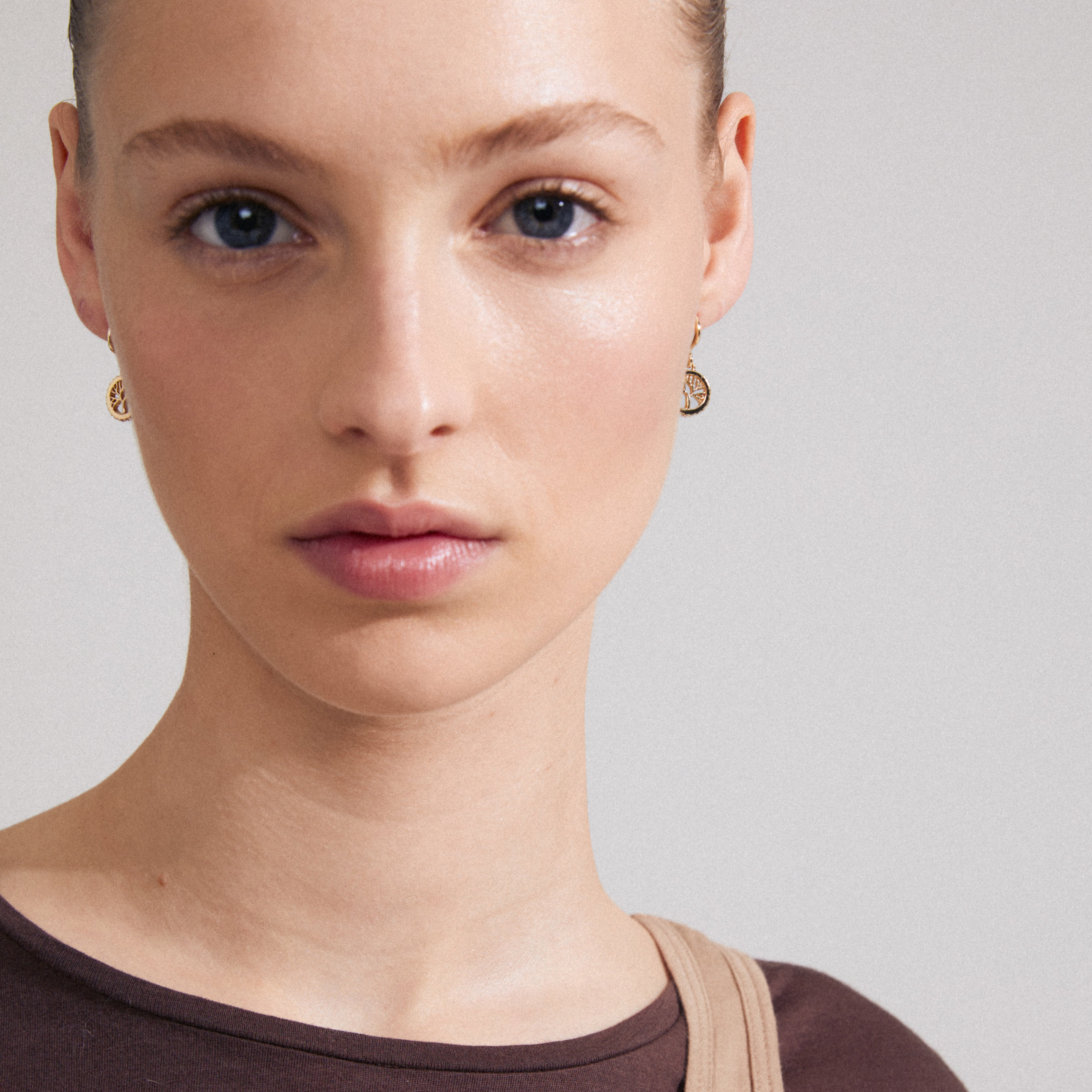 Close-up of a woman wearing ALIA gold-plated earrings with circular pendants, featuring Preciosa crystals and Tree of Life carvings, symbolizing strength and connection.