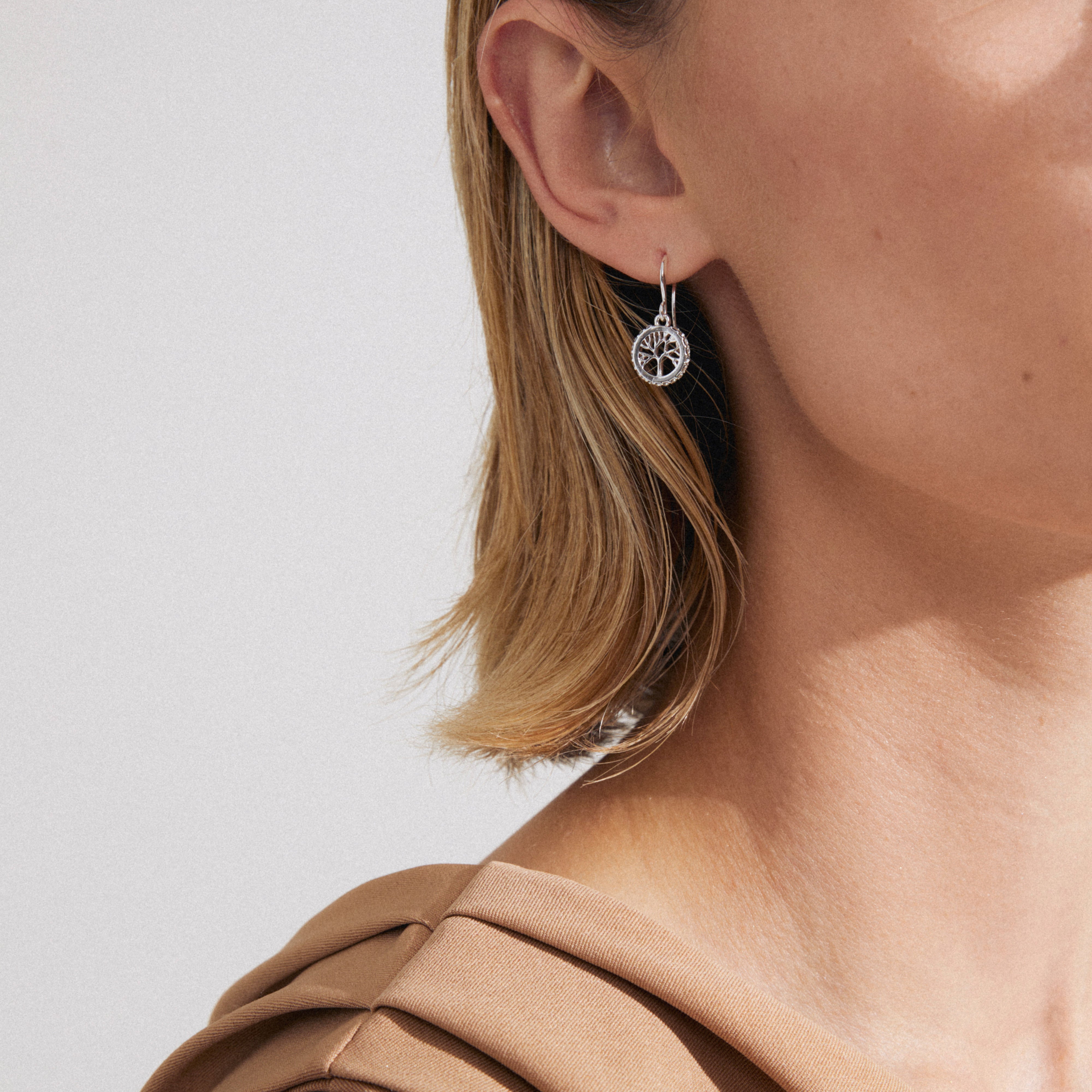 Close-up of ALIA earrings silver-plated, featuring a tree of life design with Preciosa crystals, worn by a person with short blonde hair.