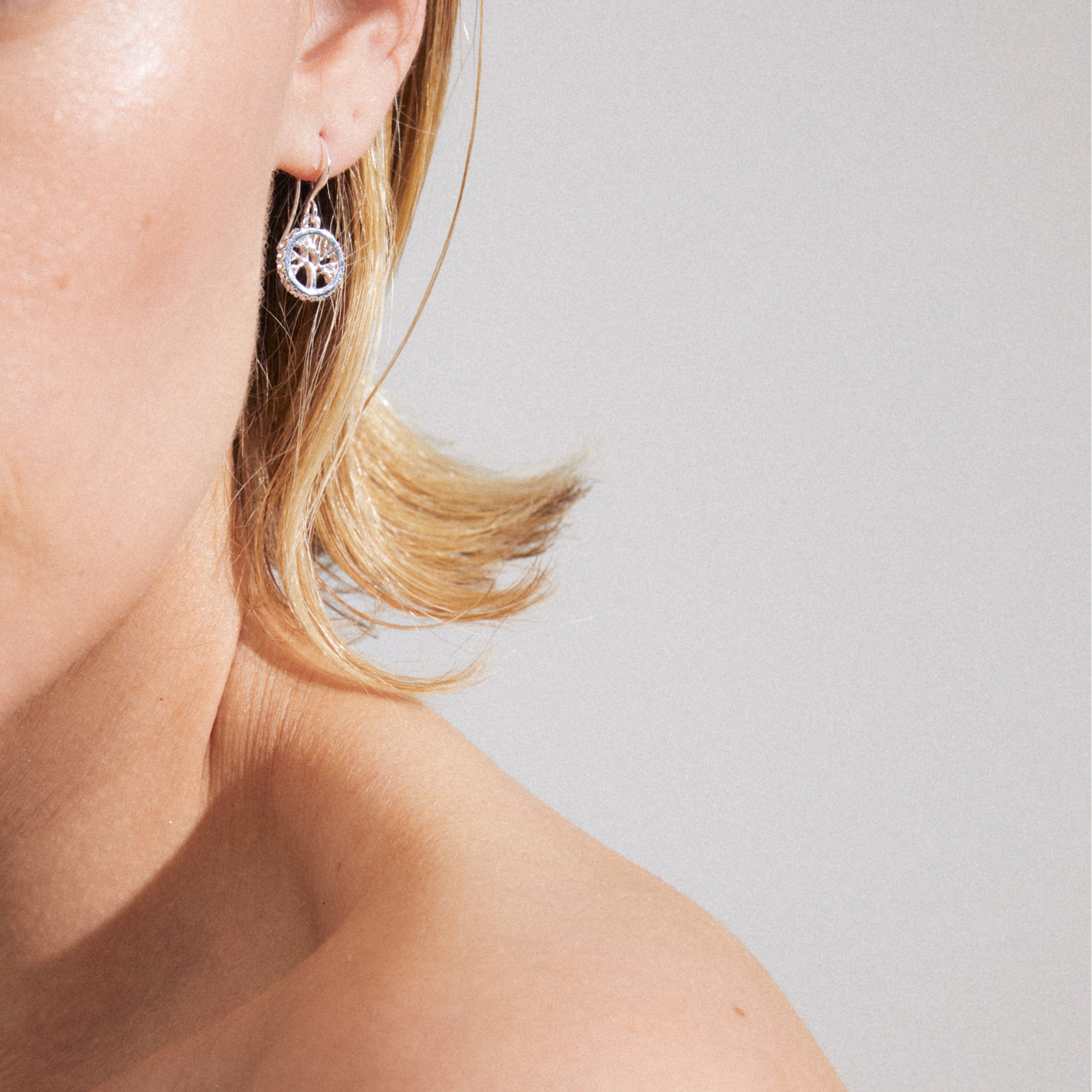 Close-up of ALIA earrings, silver-plated, featuring a Tree of Life design with Preciosa crystals, worn by a model with short, light-blonde hair.