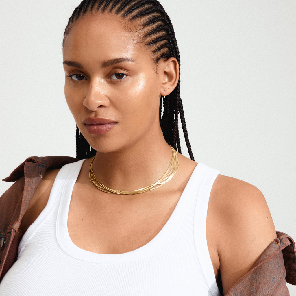 KIRA gold-plated necklace on a woman with braided hair, featuring five layered flat snake chains, showcasing a bold, sculptural design.
