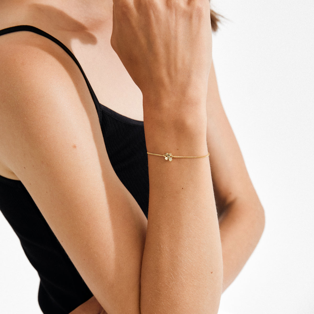 Woman wearing the AJANI bracelet gold-plated, featuring a dainty four-leaf-clover charm, highlighting its delicate and playful style against a light background.