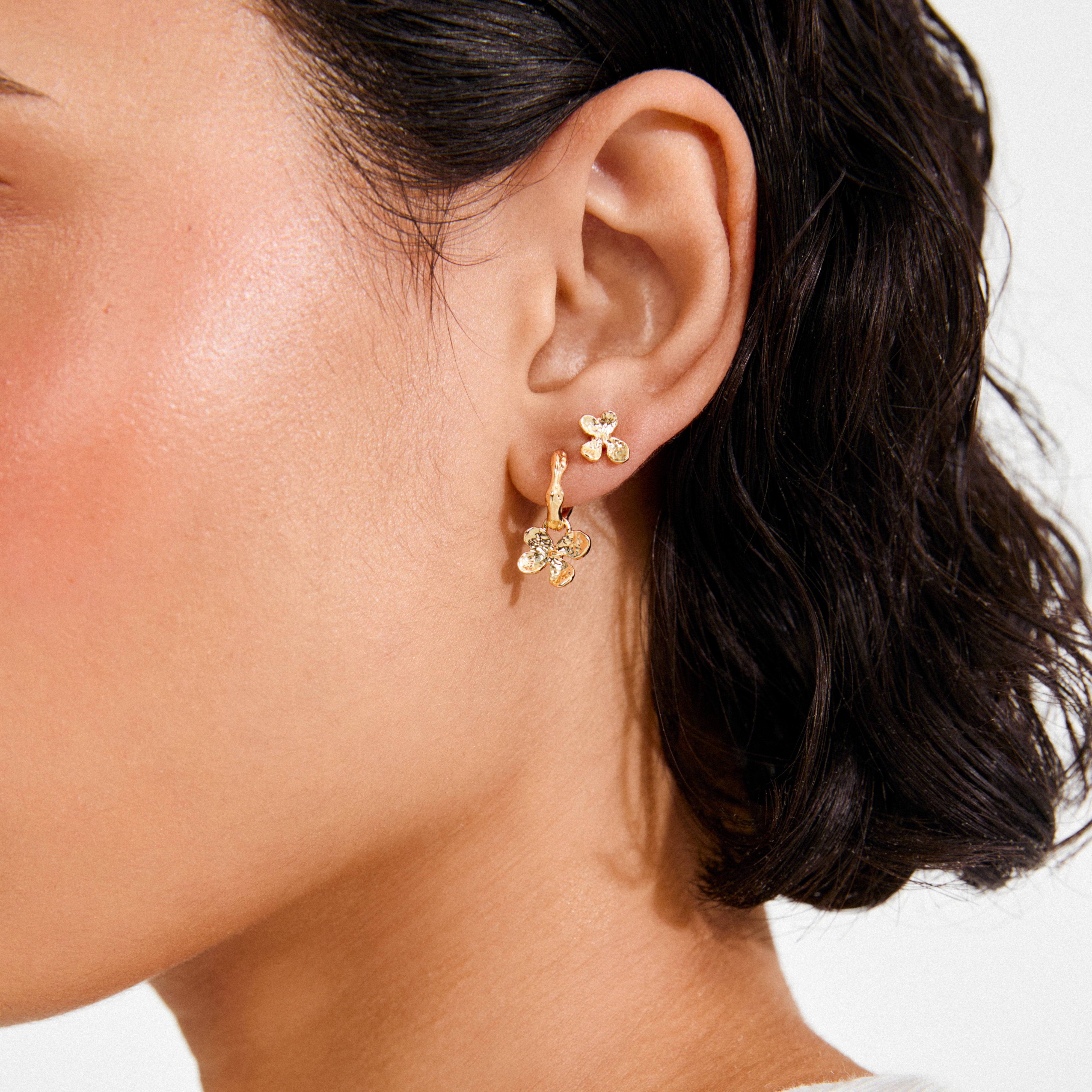 AJANI earrings 2-in-1 set: close-up of ear with a gold flower stud and hoop with matching flower charm, showcasing versatile, elegant Danish design by Pilgrim.