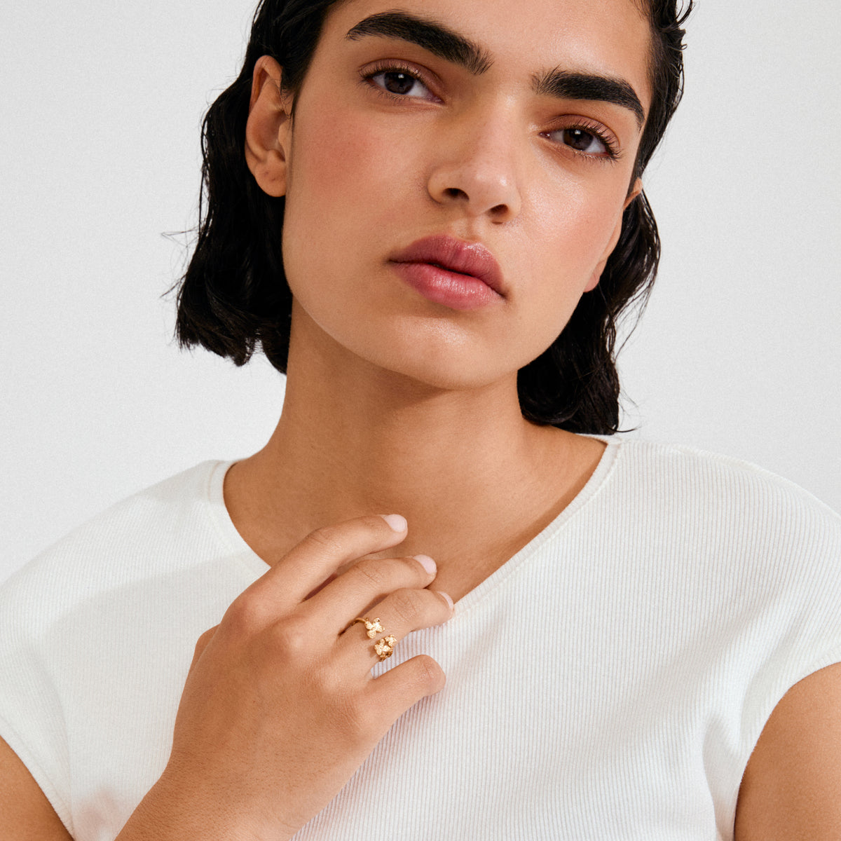 Young woman wearing Pilgrim's gold-plated AJANI ring with flower and bud motifs, showcasing its delicate, twig-inspired design on her middle finger.