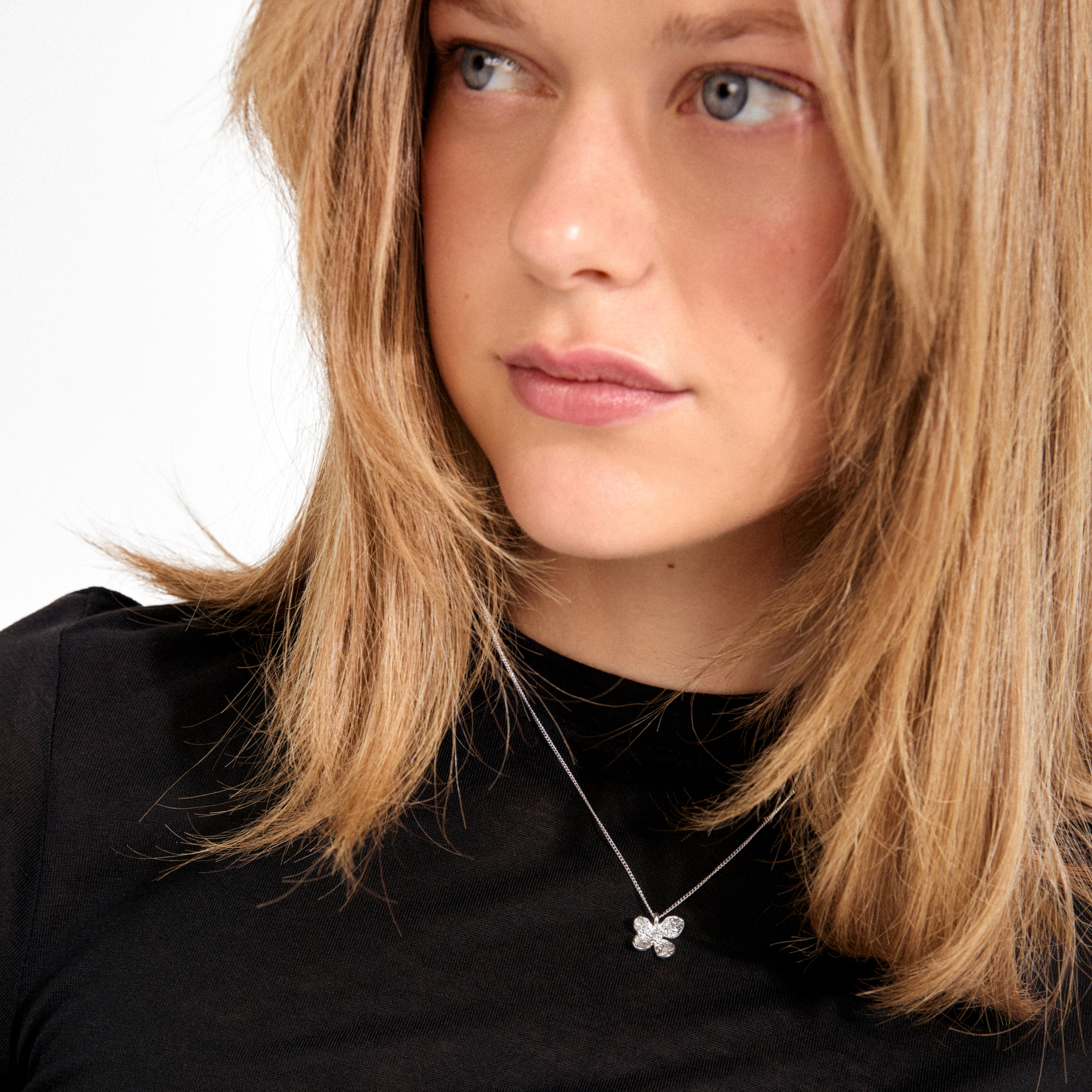 Young woman wearing Pilgrim's AJANI necklace; a silver-plated chain with a sparkling four-leaf clover pendant, showcasing nature-inspired, artisan craftsmanship.