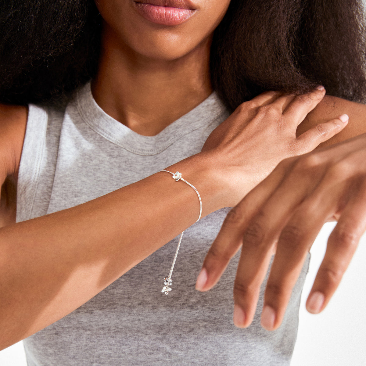 Woman wearing the silver-plated AJANI bracelet with delicate floral charms and slider-style clasp, highlighting its elegant and adjustable design on her wrist.