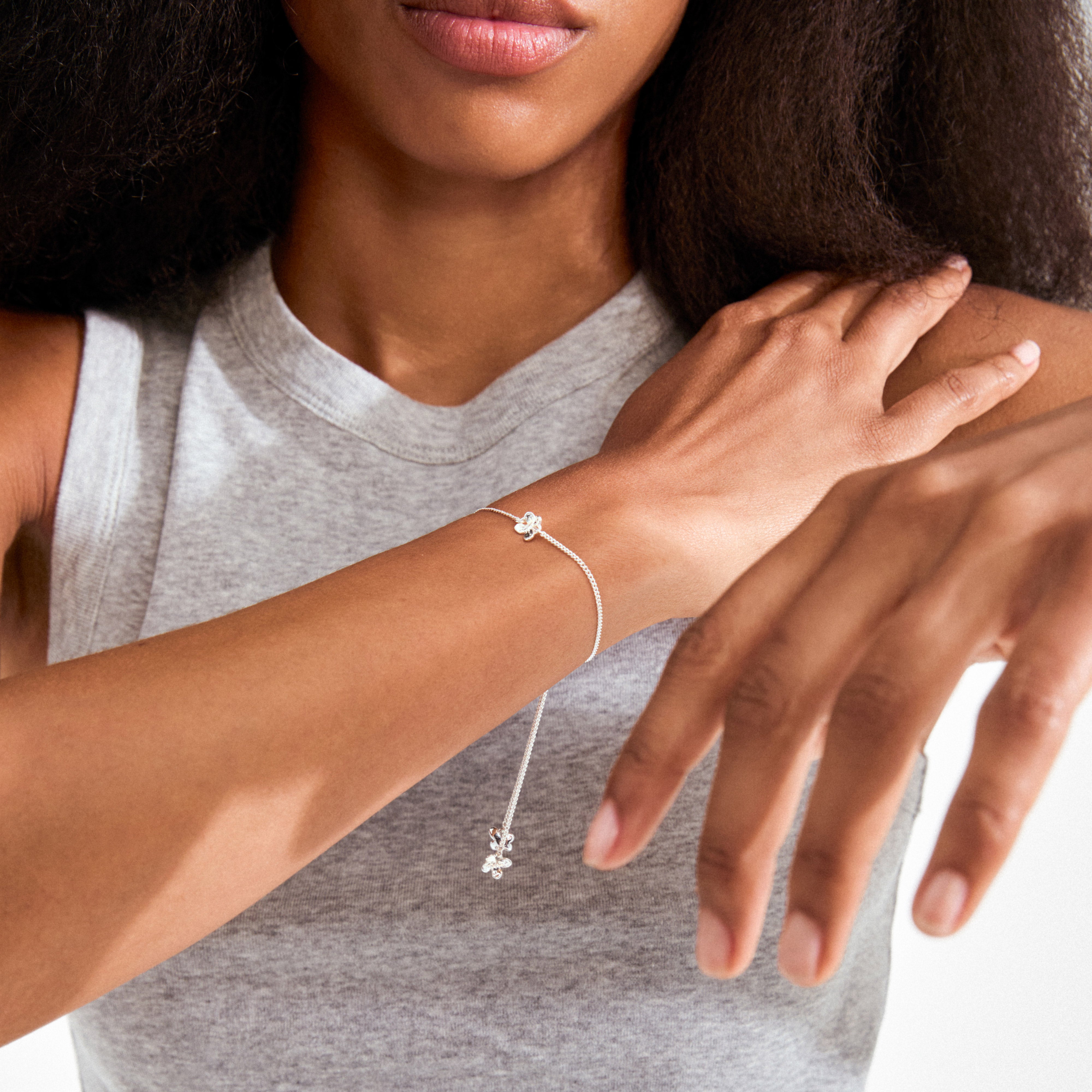 Woman wearing the silver-plated AJANI bracelet with delicate floral charms and slider-style clasp, highlighting its elegant and adjustable design on her wrist.