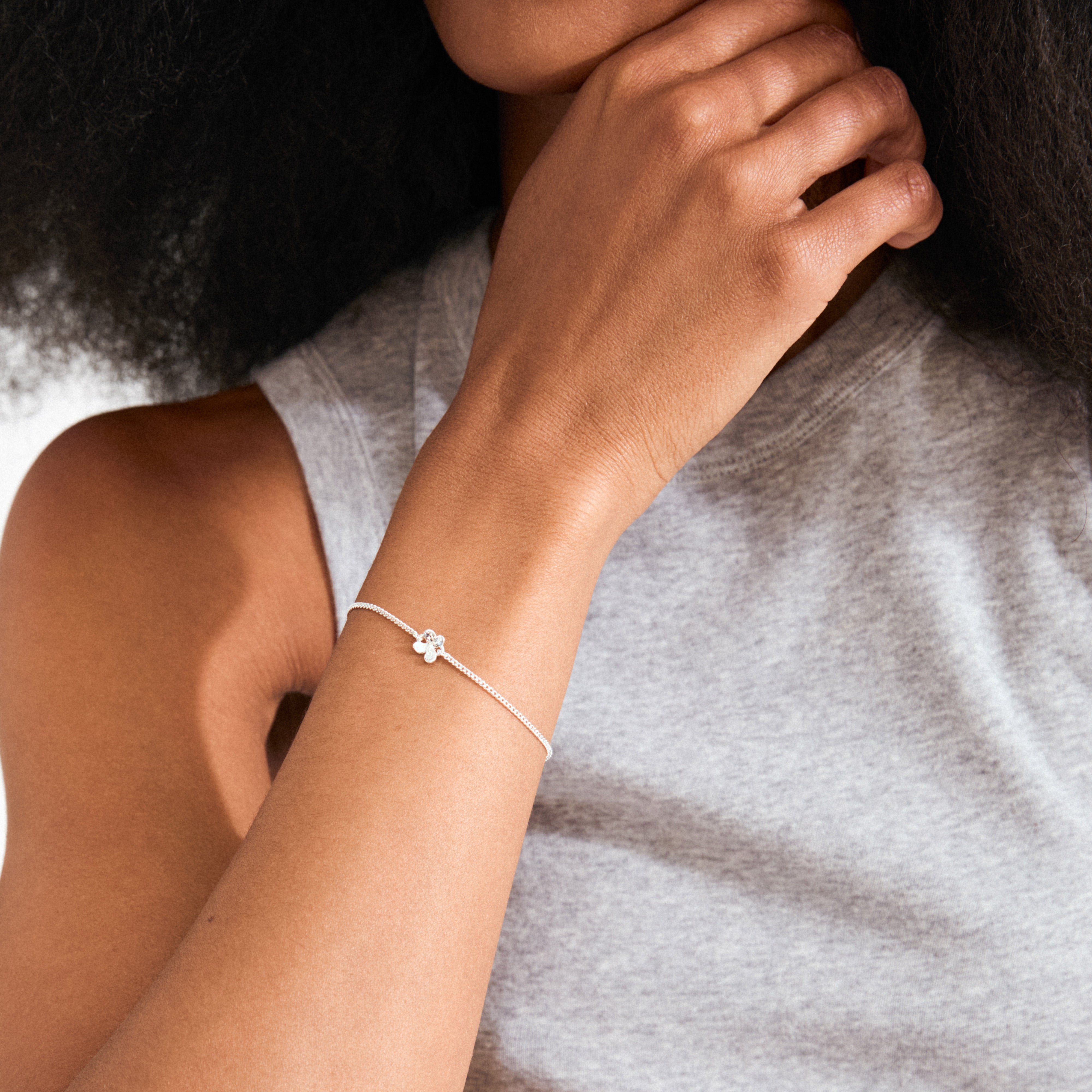 AJANI bracelet silver-plated on wrist, featuring a delicate four-leaf-clover charm and sleek chain, capturing a light, airy style with adjustable comfort.