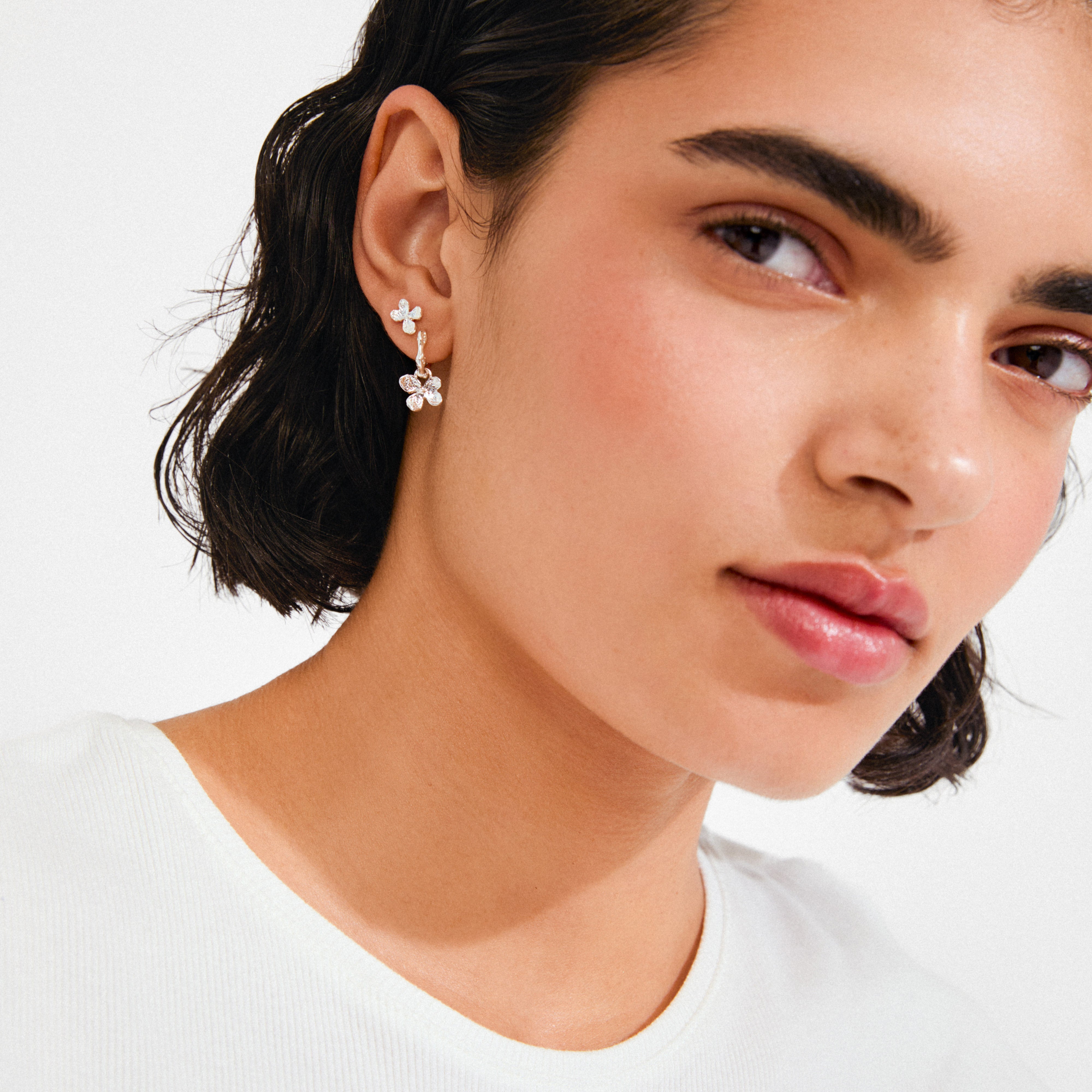 Close-up of person wearing the AJANI earrings 2-in-1 set, featuring a silver-plated flower stud and dangling charm, showcasing Pilgrim's elegant, recycled jewelry design.